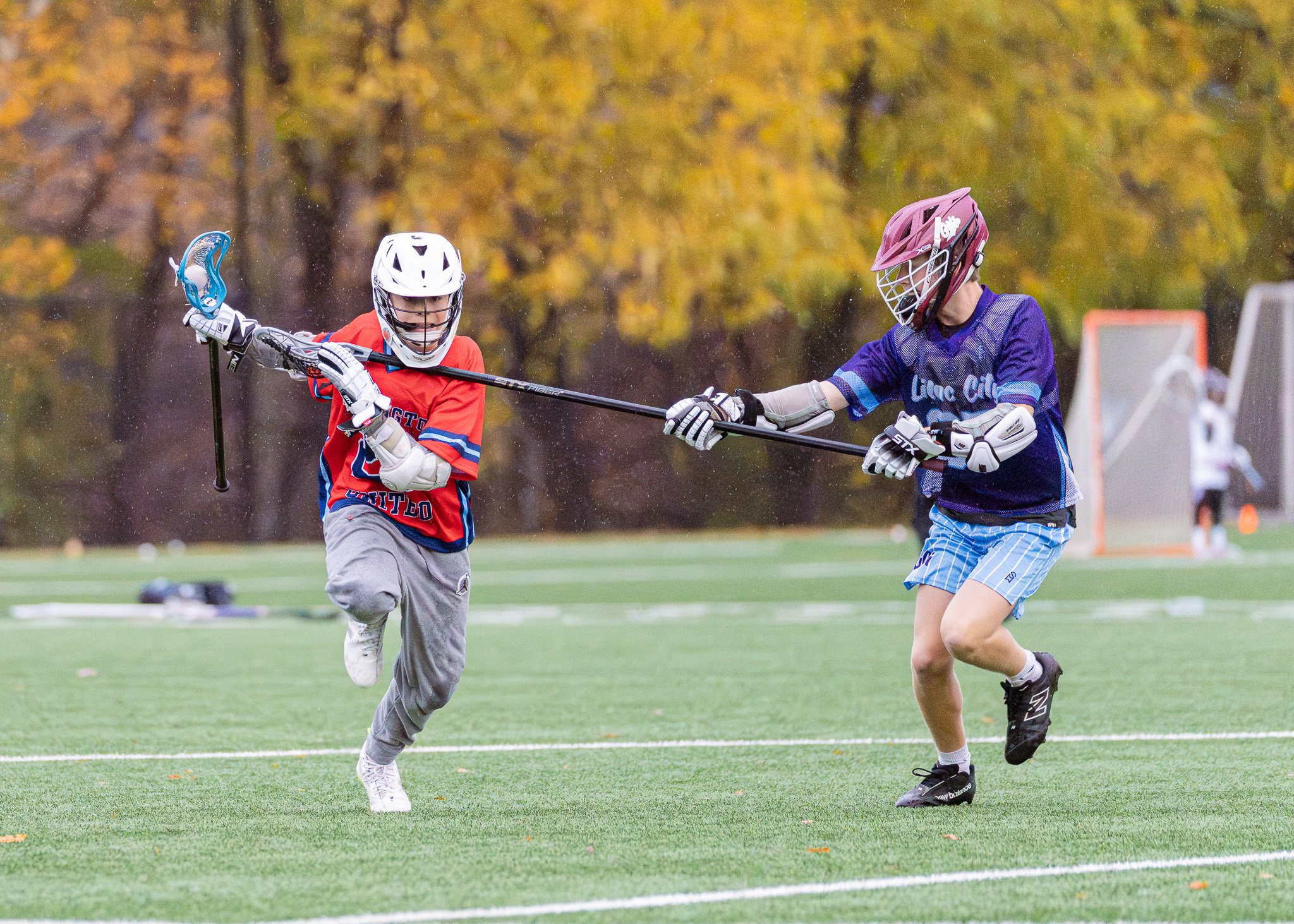Two middle school lacrosse players are competing in the rain. The defender is checking the attackman on his chest.