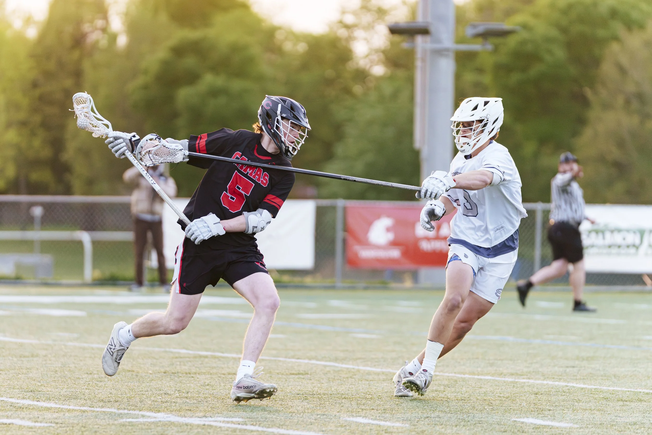 A high school lacrosse defender checks an attacker across the chest.