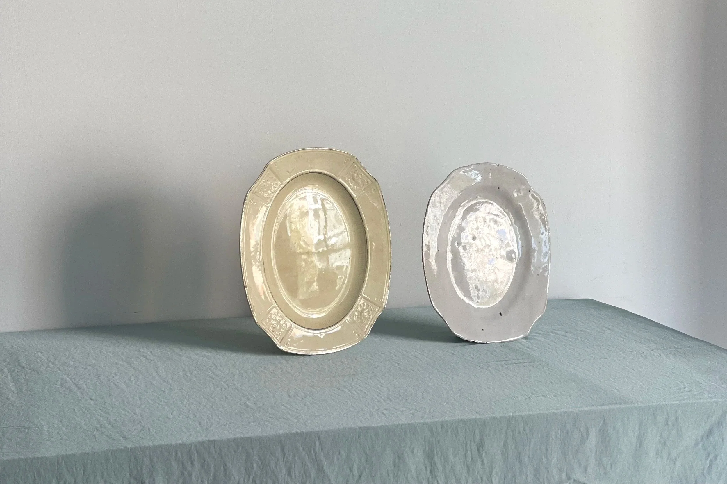 Tres platos decorativos en diferentes tamaños en tonos claros sobre una repisa blanca, con fondo gris.