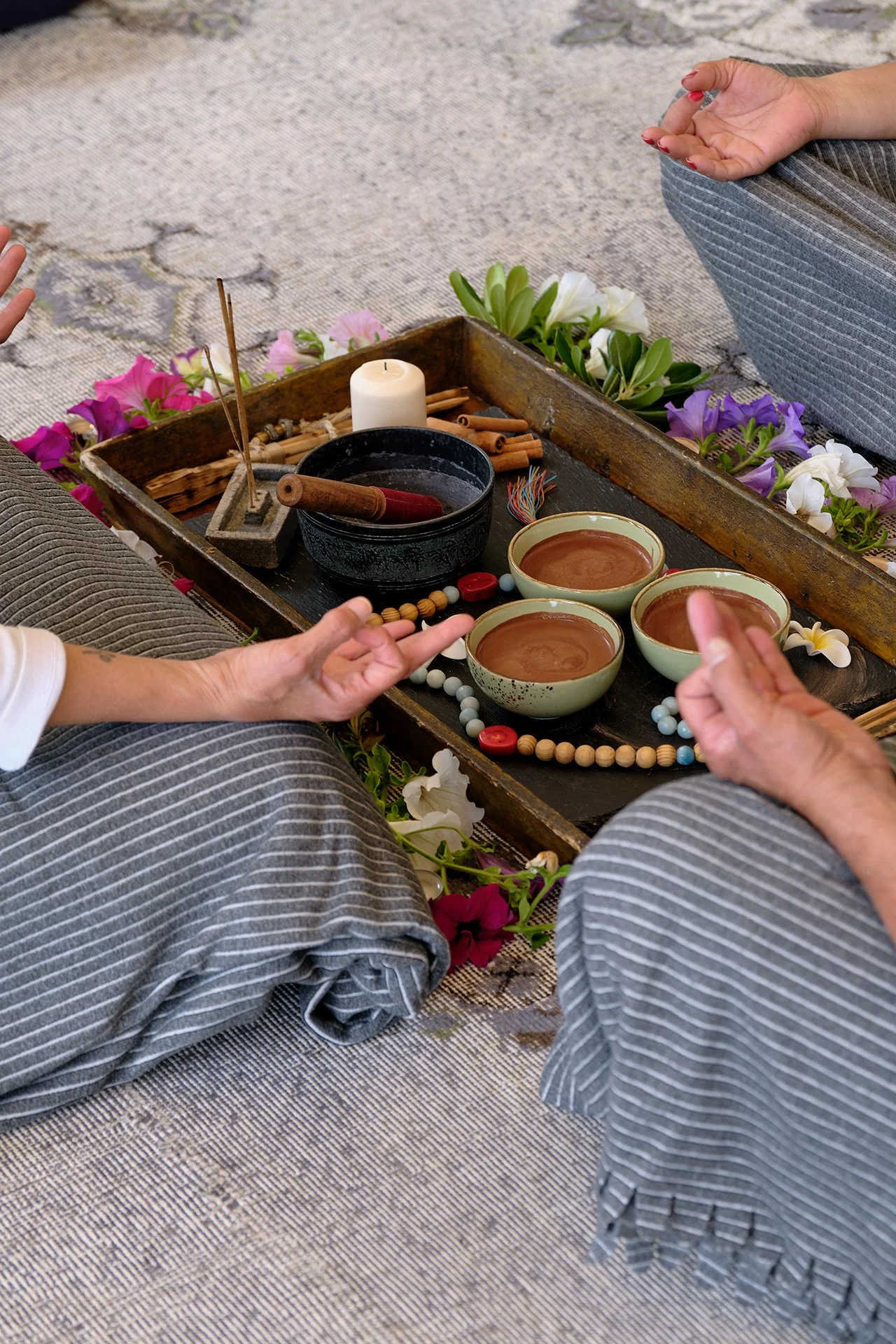 Two people sitting on the floor in meditation with a tray of tea, candles, and flowers between them.