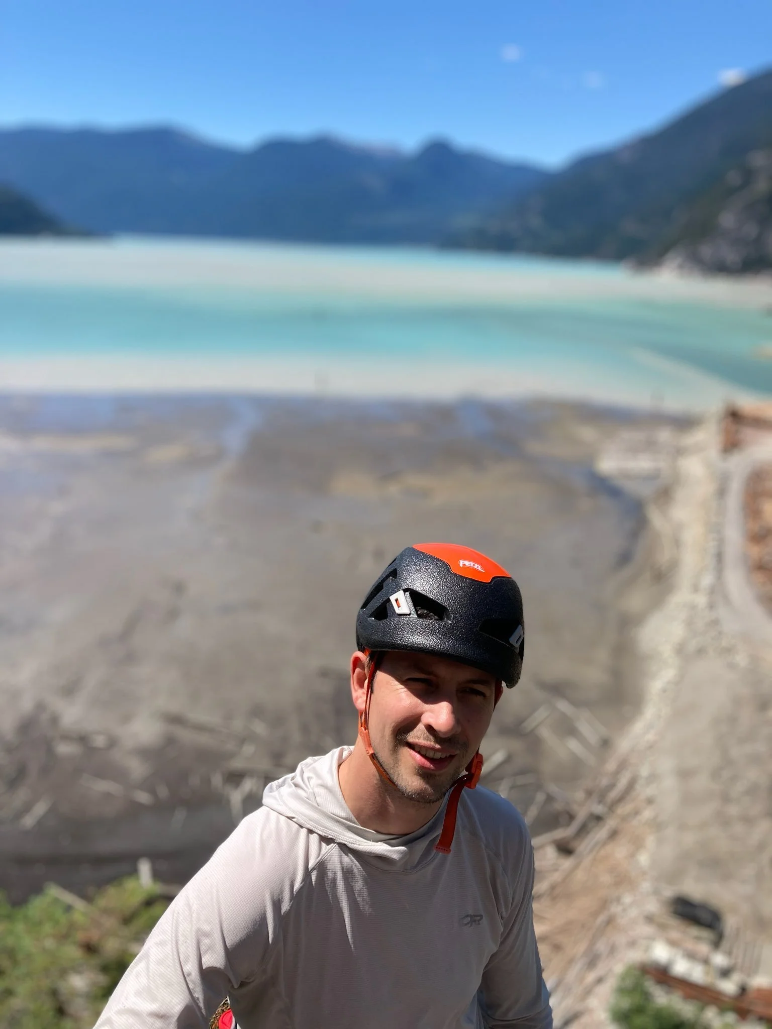 Man wearing a helmet standing in front of a scenic mountain lake view