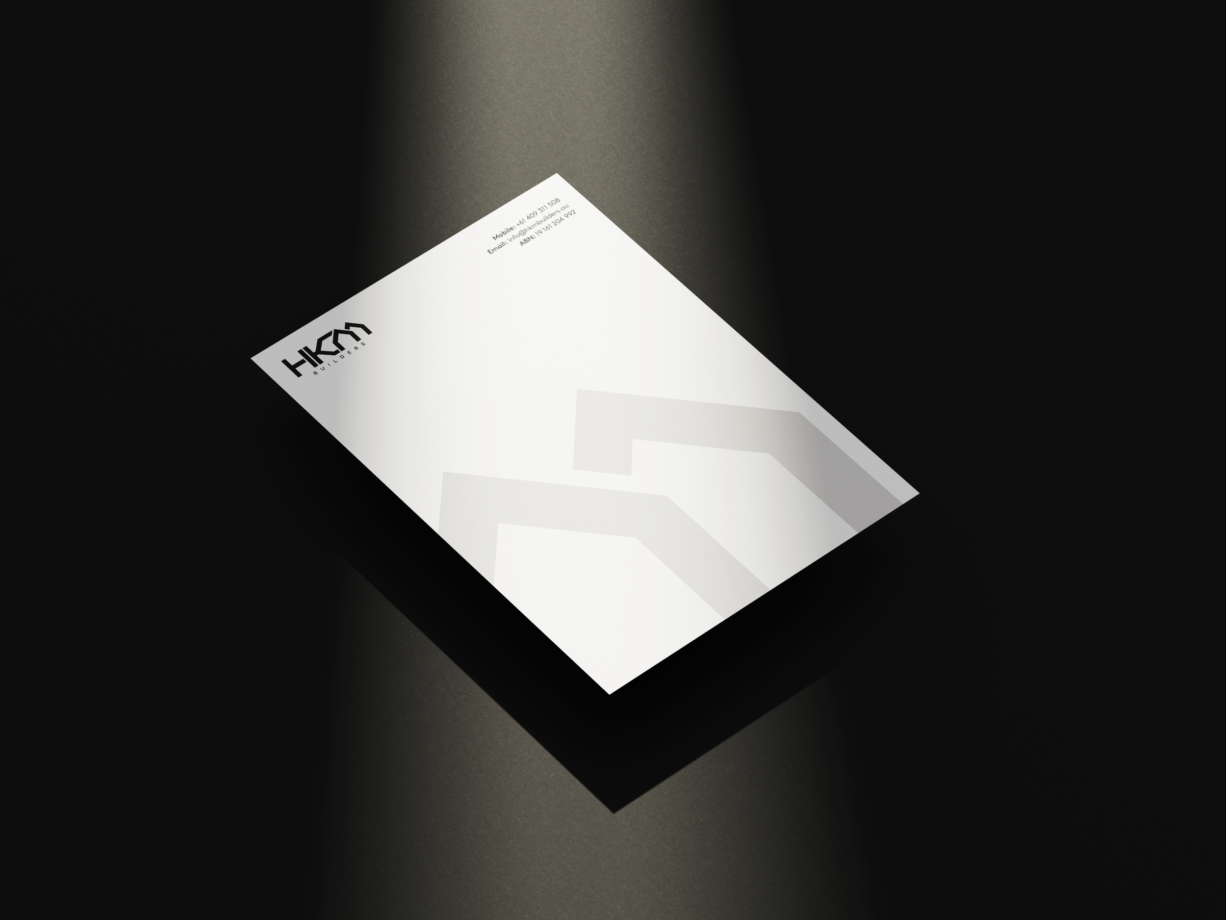 A white sheet of paper with the logo 'HKDN' on the top left corner, lying on a dark surface, partially illuminated.
