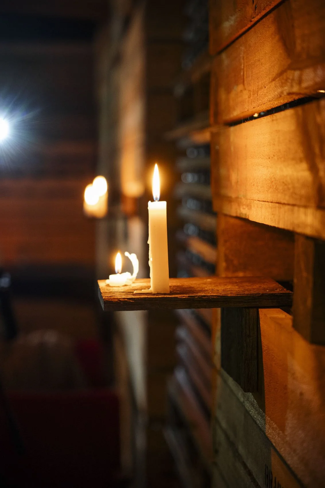 A wooden wall with lit candles on a small wooden shelf, creating a warm, cozy atmosphere.