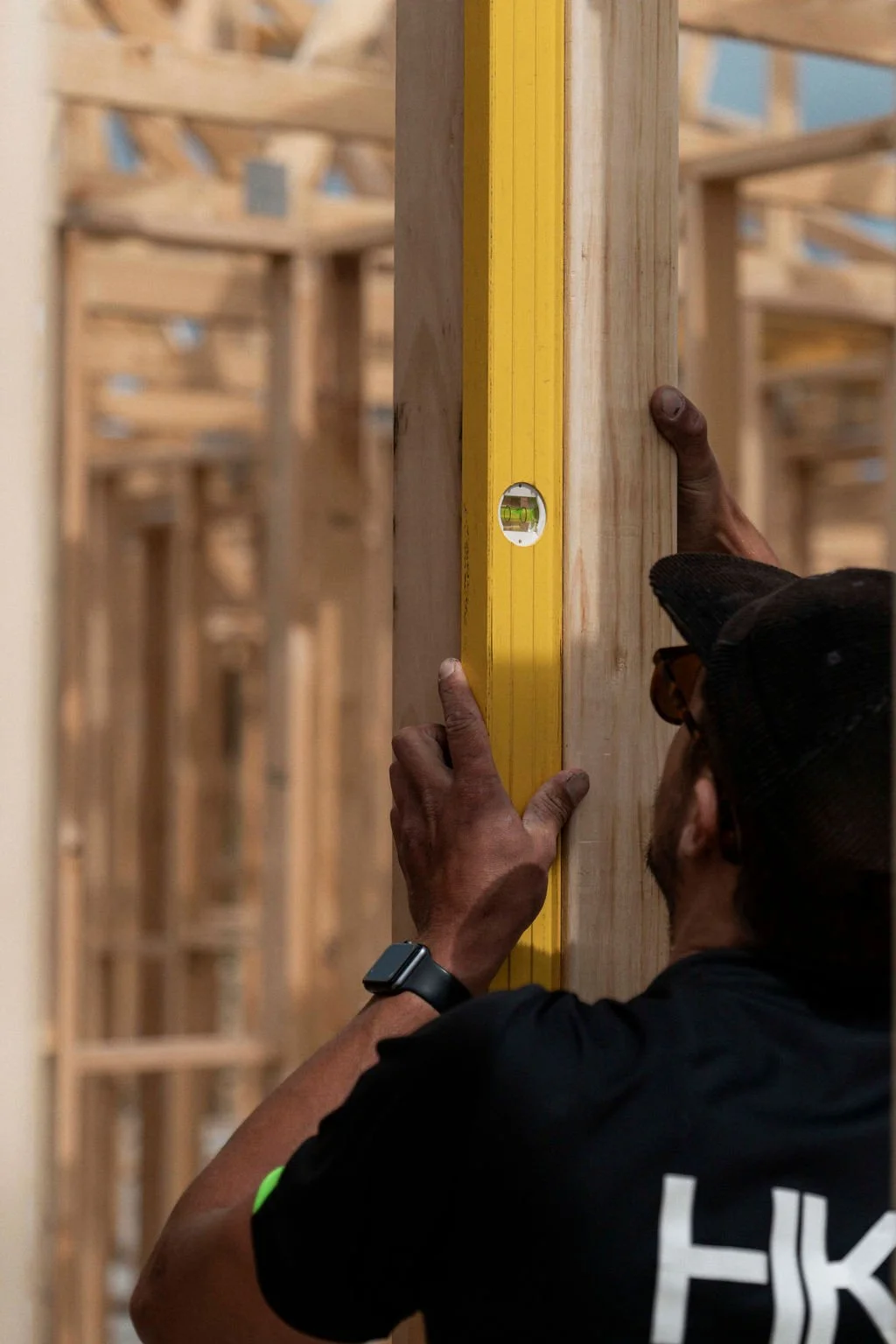 A construction worker uses a yellow level to ensure a wooden wall stud is straight at a building site