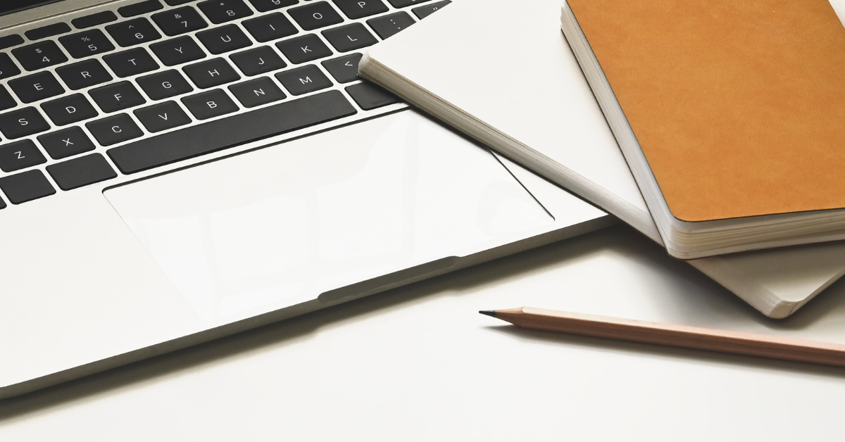 Close up of a laptop keyboard with two stacked notebooks resting on the corner and a sharpened wooden pencil placed on the desk. The simple arrangement highlights a tidy workspace ready for writing or planning tasks.
