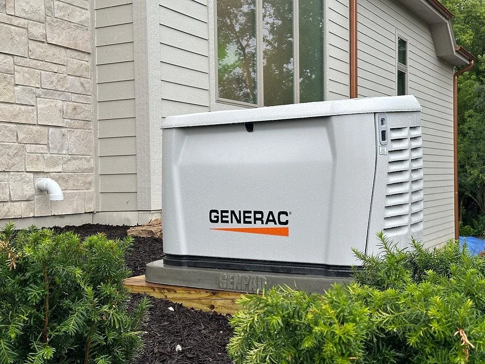 A Generac backup generator installed outside a house on a wooden platform, surrounded by green bushes.