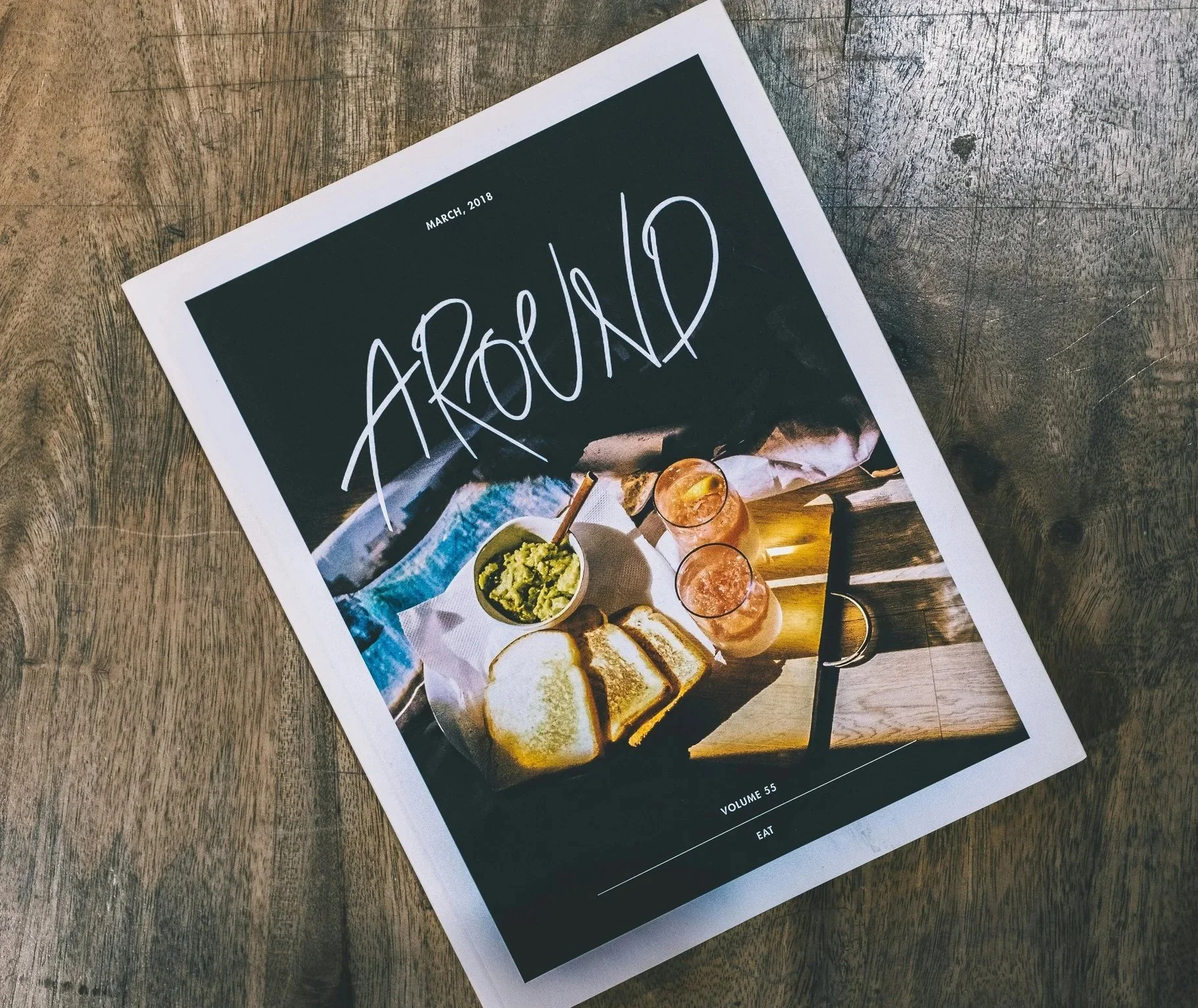 A magazine titled "AROUND" from March 2018 featuring a breakfast scene on a wooden table with toast, guacamole, and drinks.