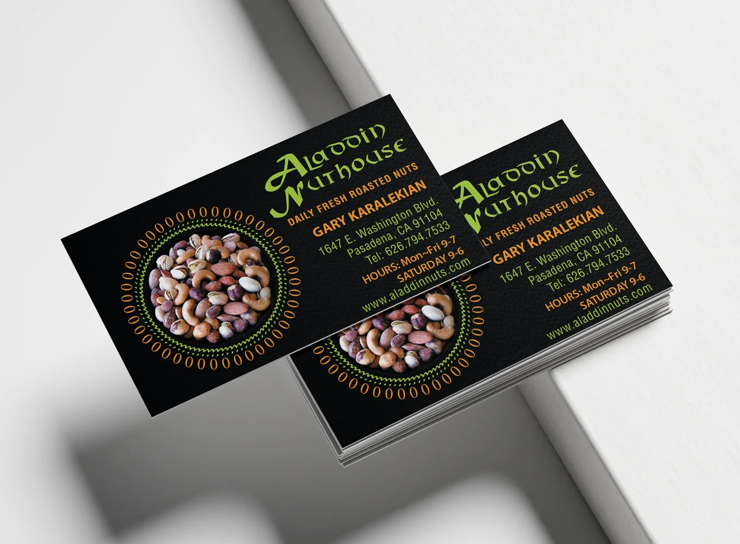 Stack of business cards for Aladdin Muthouse with a black background, a circular image of mixed roasted nuts, and green and orange text displaying the business name, address, phone number, hours, and website.