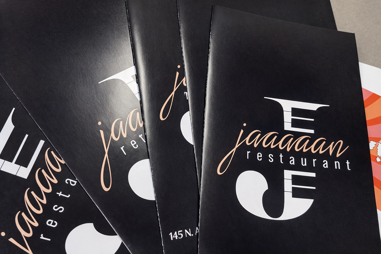 Close-up of black menus for Jaaaan restaurant, showing the restaurant's logo and address at 145 N. Broadway.