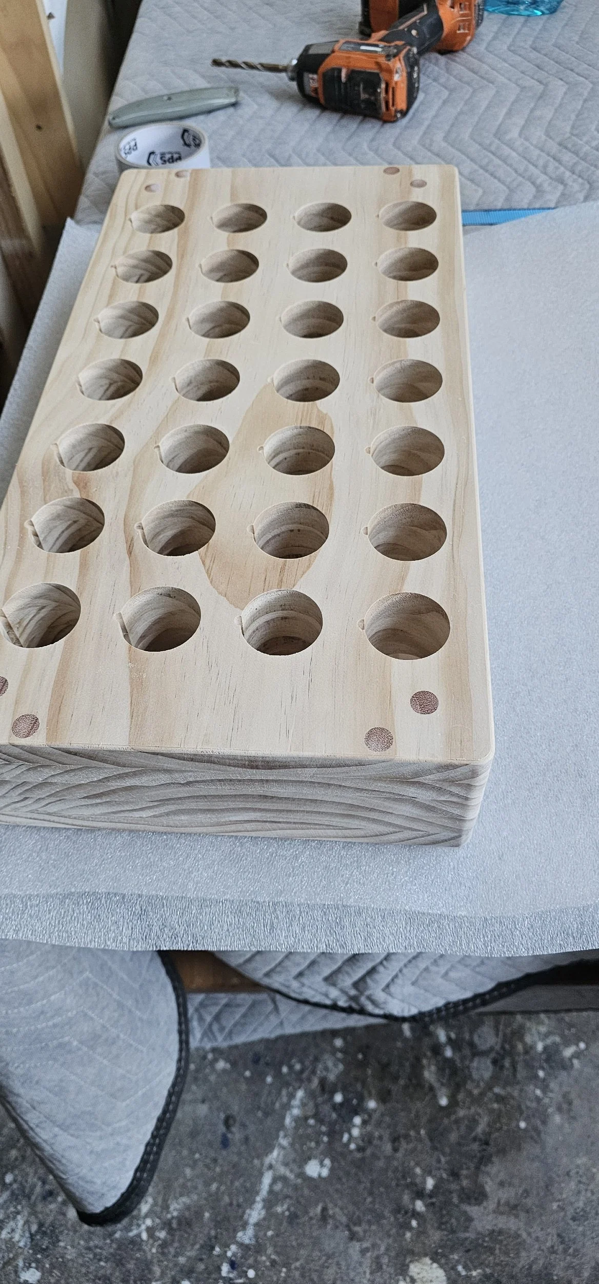 Unfinished wooden block with multiple circular cutouts for custom use, on a work table with tools and supplies.