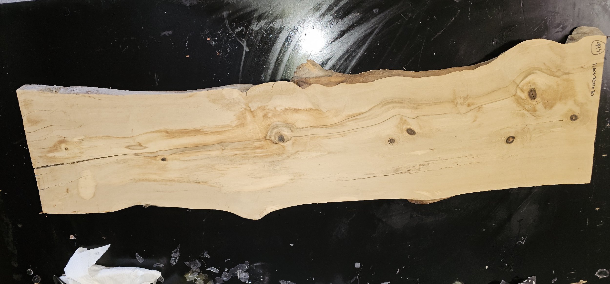 A long, uneven, natural olive wood plank with knots and cracks on a black surface.