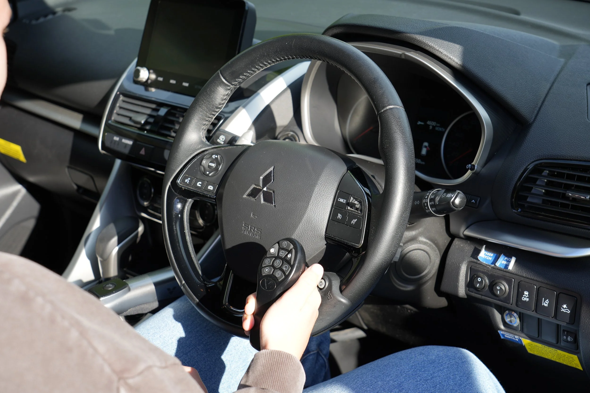 Person holding the modified steering wheel of a car during a occupational therapy driving assessment.