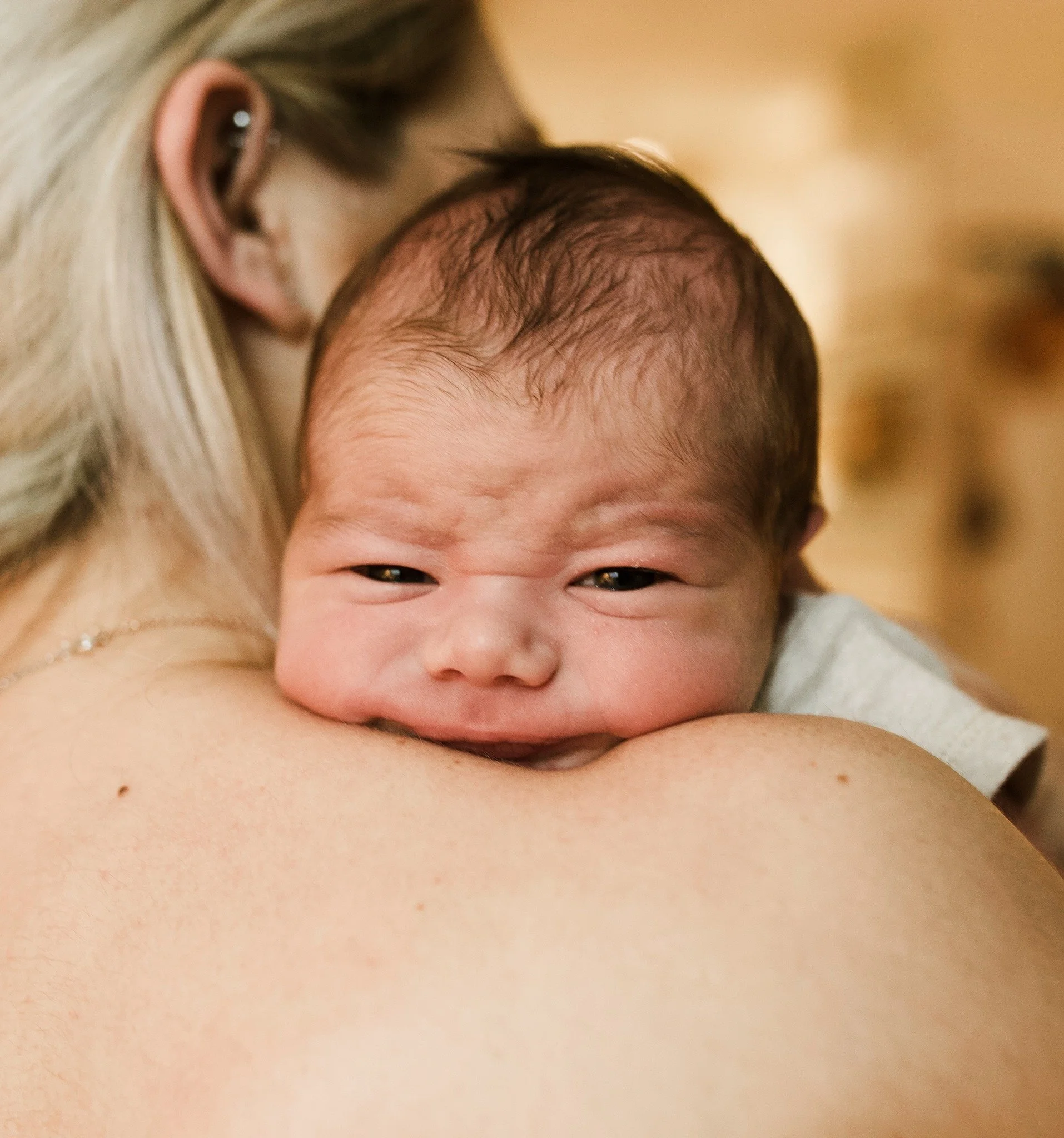 Close-up of a smiling woman resting her head on the arm of a person, showing her face and hair with a blurred background.