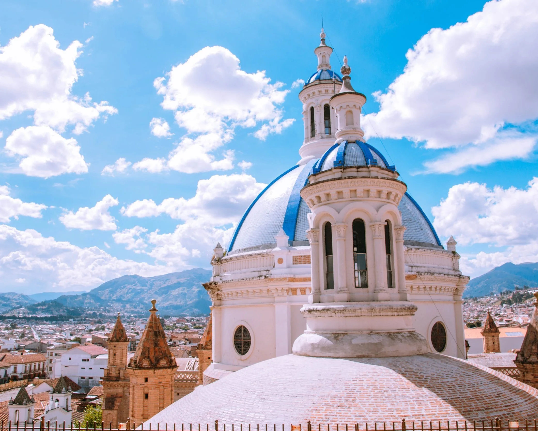 White towers and blue tiled domes of the New Cathedral of Cuenca rising above the colonial rooftops with Andean mountains in the background, Ecuador