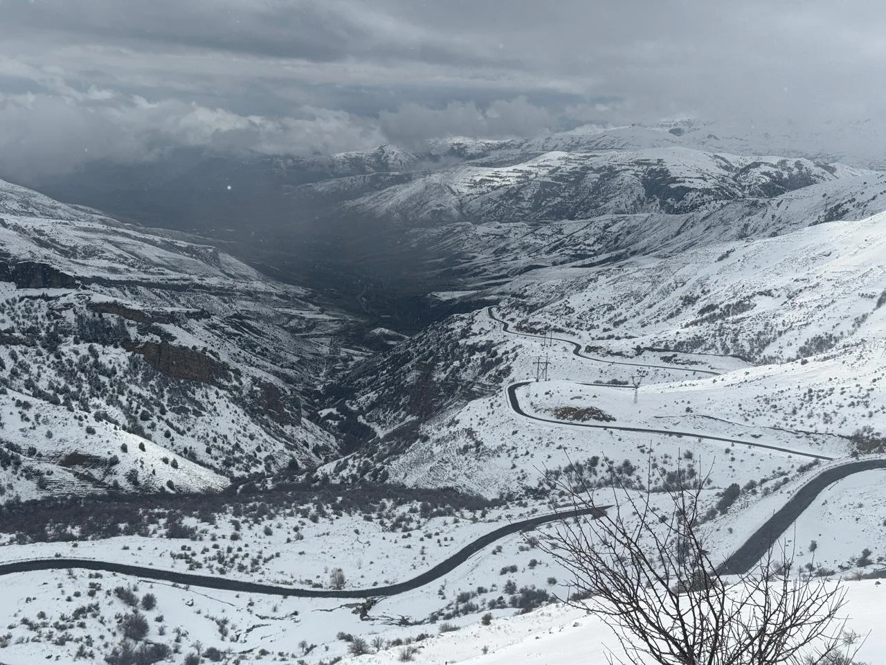 Wide mountain valley blanketed in snow with a winding road cutting through the Lesser Caucasus landscape in Armenia under a dramatic overcast sky