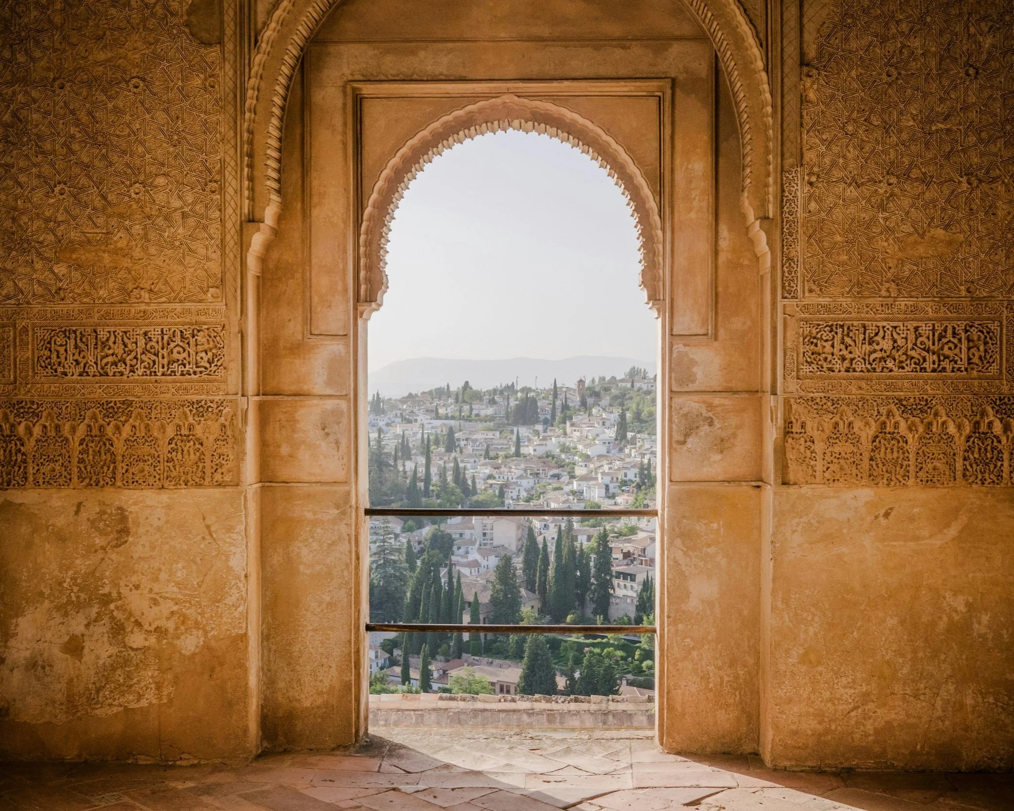 View through an ornate Moorish horseshoe arch in the Alhambra palace complex overlooking the white rooftops and gardens of Granada, Andalucía, Spain