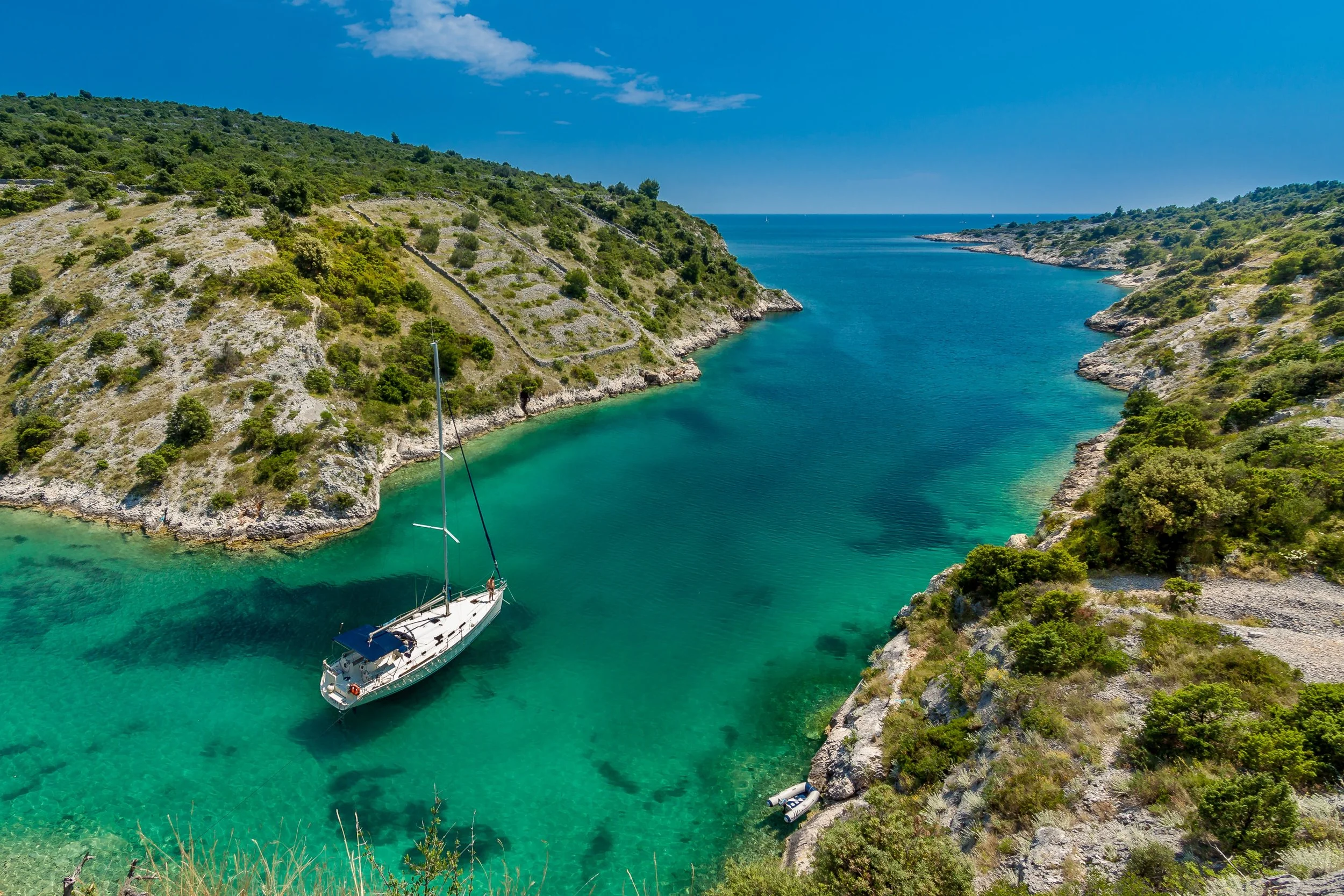 A private sailing yacht anchored in a secluded turquoise cove between forested islands in the Croatian Adriatic, accessible only by private vessel