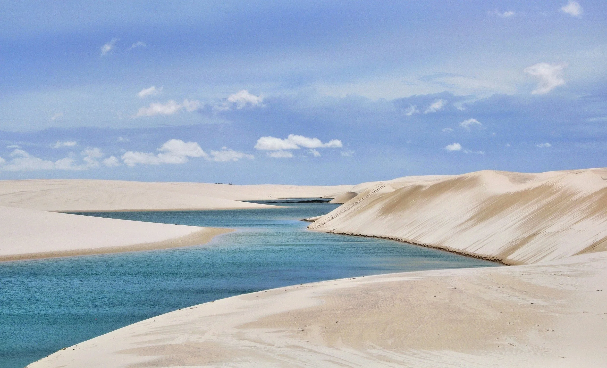 Turquoise rainwater lagoon set among rolling white sand dunes in the Lençóis Maranhenses desert landscape, Brazil