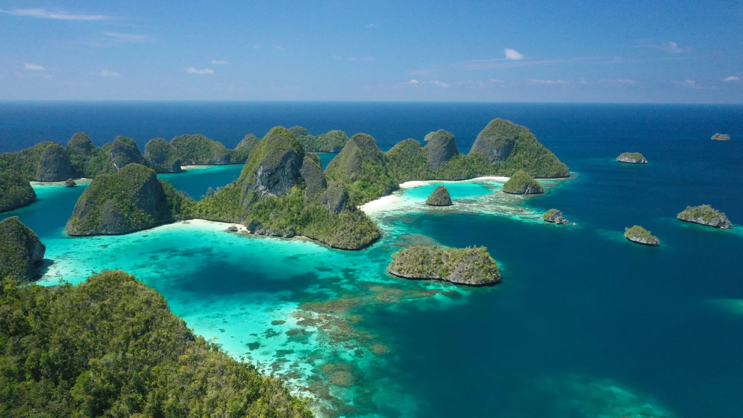 Aerial view of the forested limestone islands of Raja Ampat rising from brilliant turquoise and deep blue waters in West Papua, Indonesia