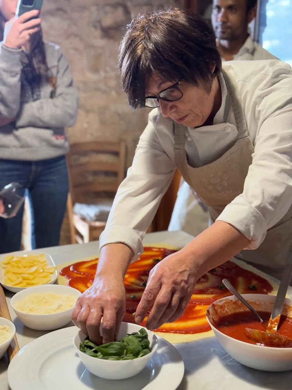 A woman working with fresh pasta dough at a table of traditional Italian dishes including tomato sauce and polenta during a private cooking class in Italy