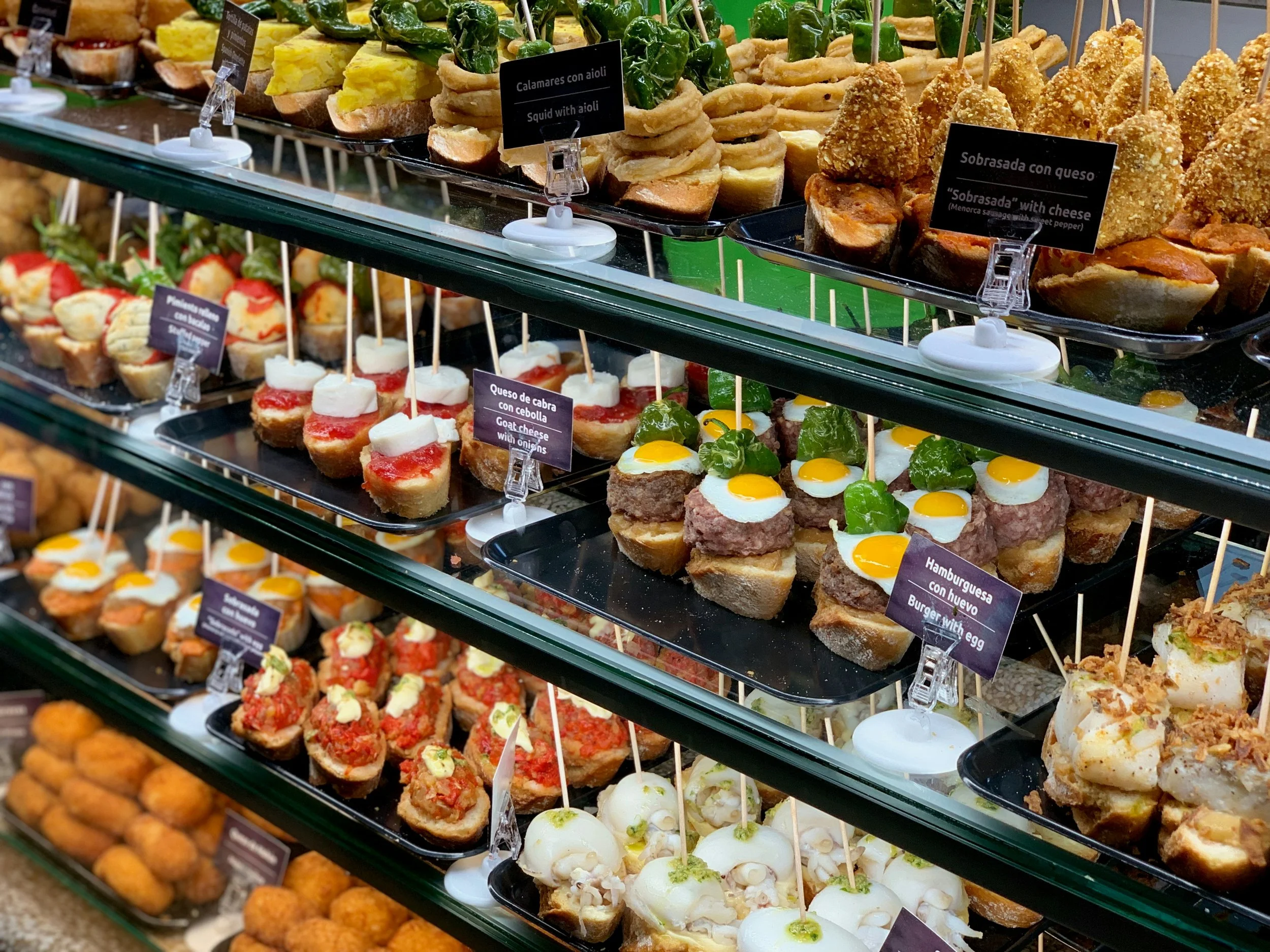 Rows of elaborate pintxos on bread displayed along a bar counter in San Sebastián, the Basque Country, showcasing Spain's world-renowned food culture