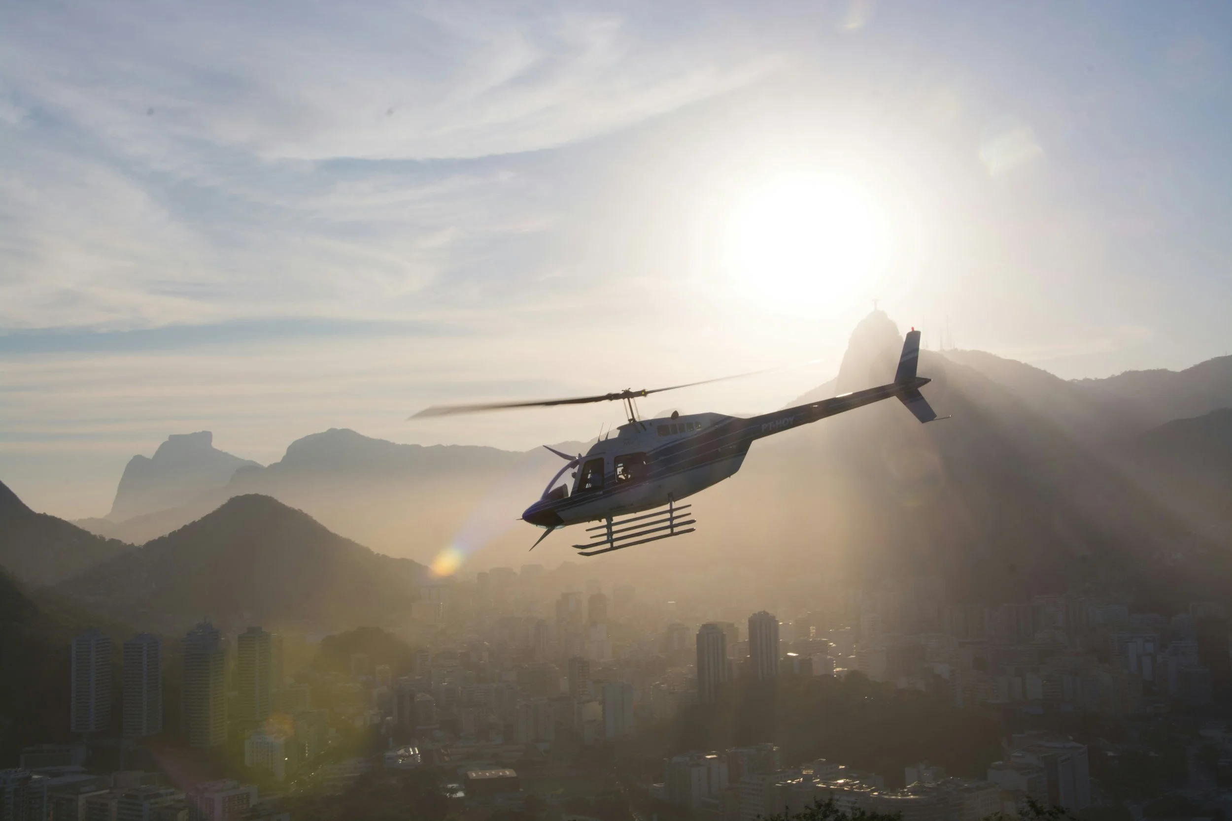Private helicopter flying above the hazy skyline of Rio de Janeiro at sunrise with mountains silhouetted in the background, Brazil
