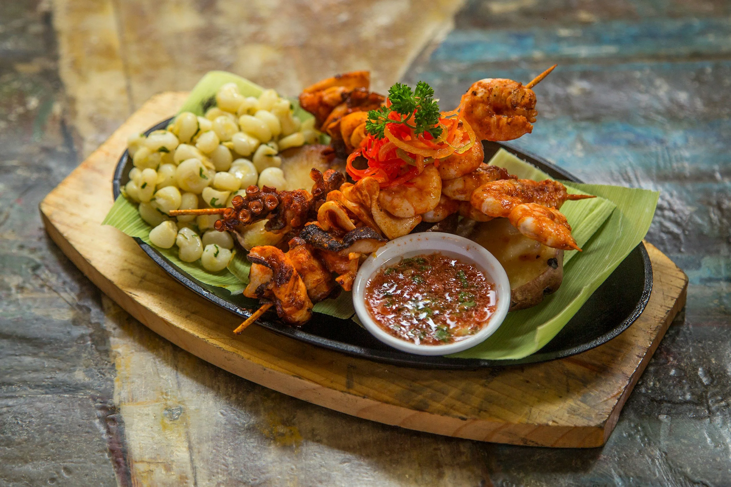 Grilled seafood and anticucho skewers served with choclo corn on a wooden board at a Lima street food experience, Peru