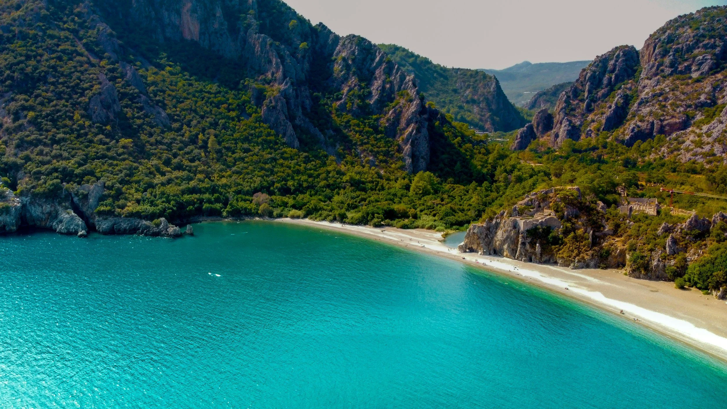 Aerial view of a secluded turquoise bay flanked by pine-covered mountains on the Turkish Riviera, Turkey