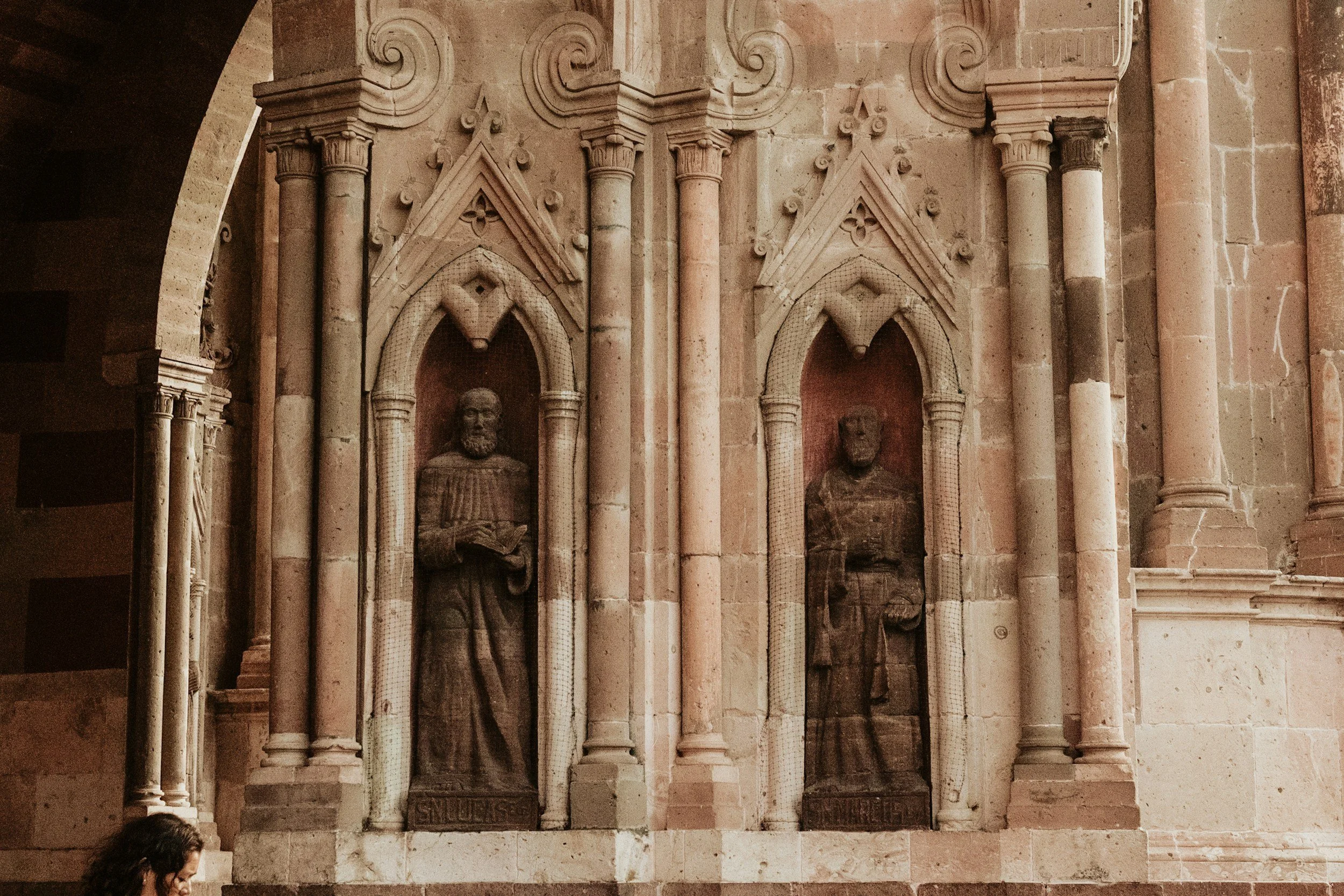 Stone religious sculptures set into Gothic arched niches on the facade of a colonial church in San Miguel de Allende, Mexico