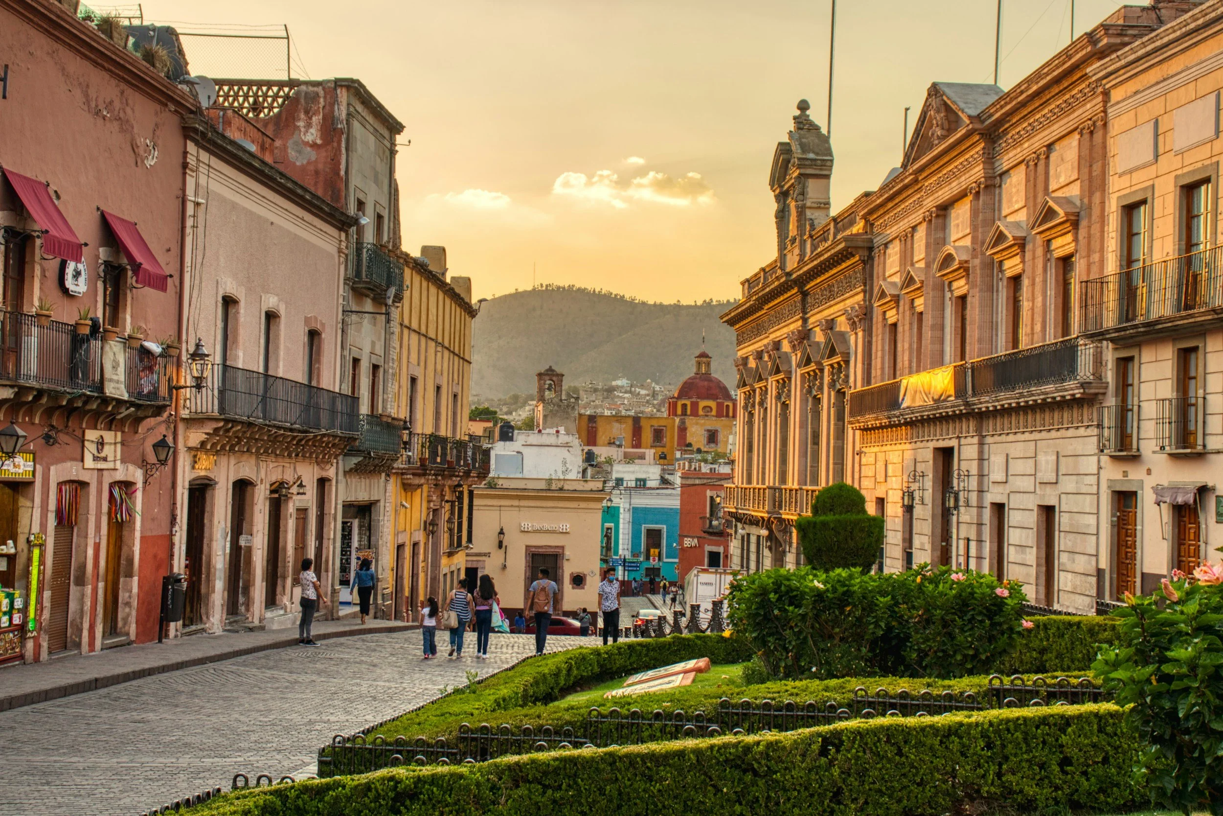 Pedestrians walking along a colonial street in San Miguel de Allende at golden hour with a mountain visible in the background, Mexico
