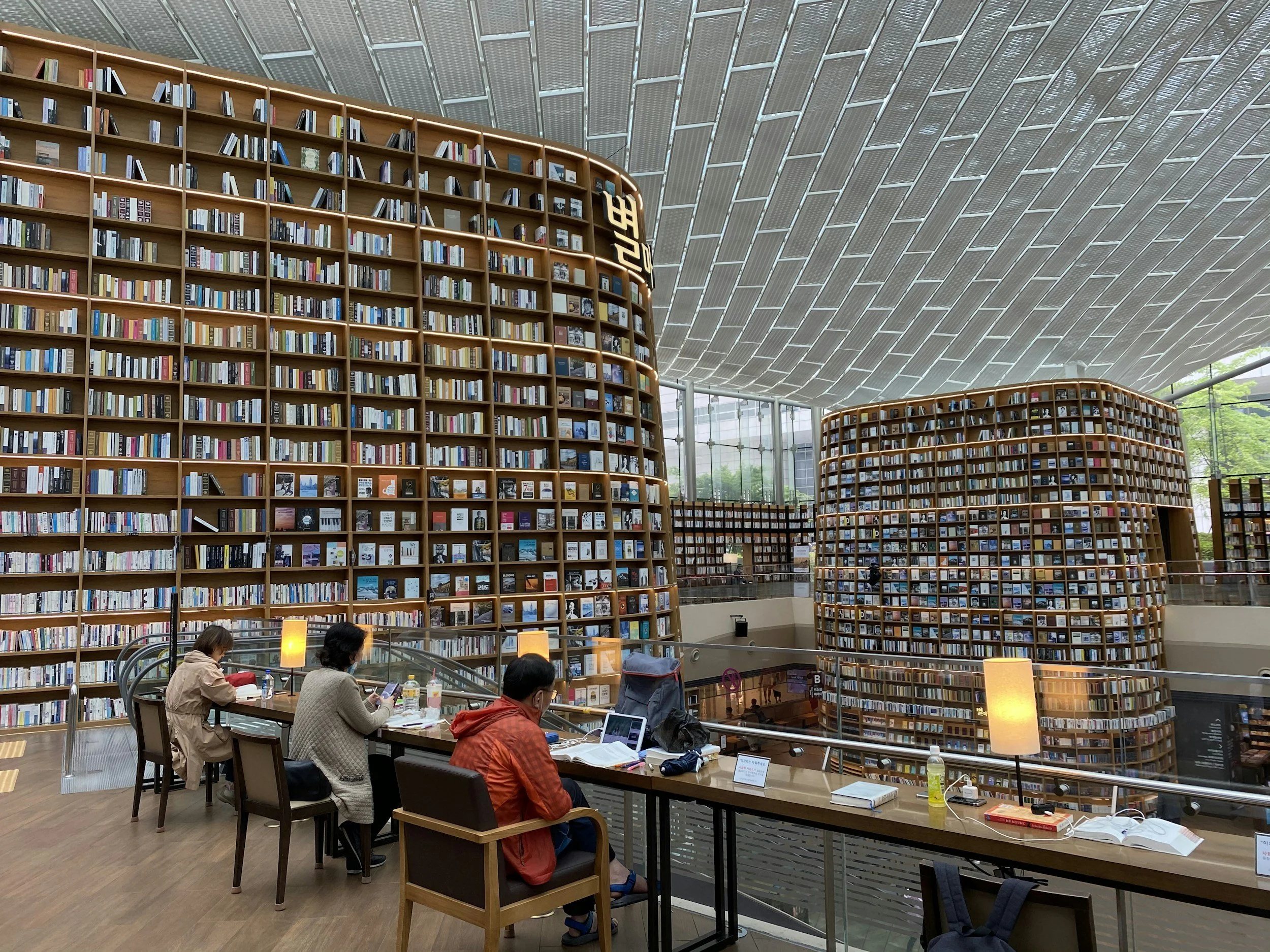 Towering curved bookshelves filled with thousands of books inside the Starfield Library at COEX Mall in Gangnam, Seoul, with visitors reading and working at tables below