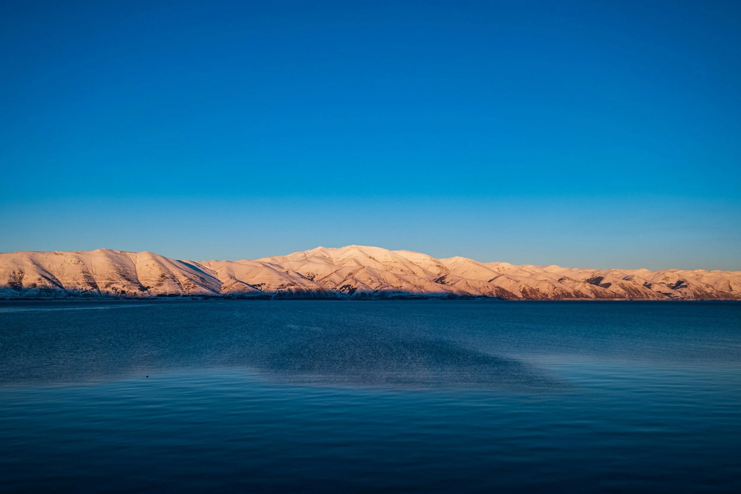 Calm deep-blue waters of Lake Sevan with arid mountain ridges reflected on the surface under a clear blue sky in Armenia