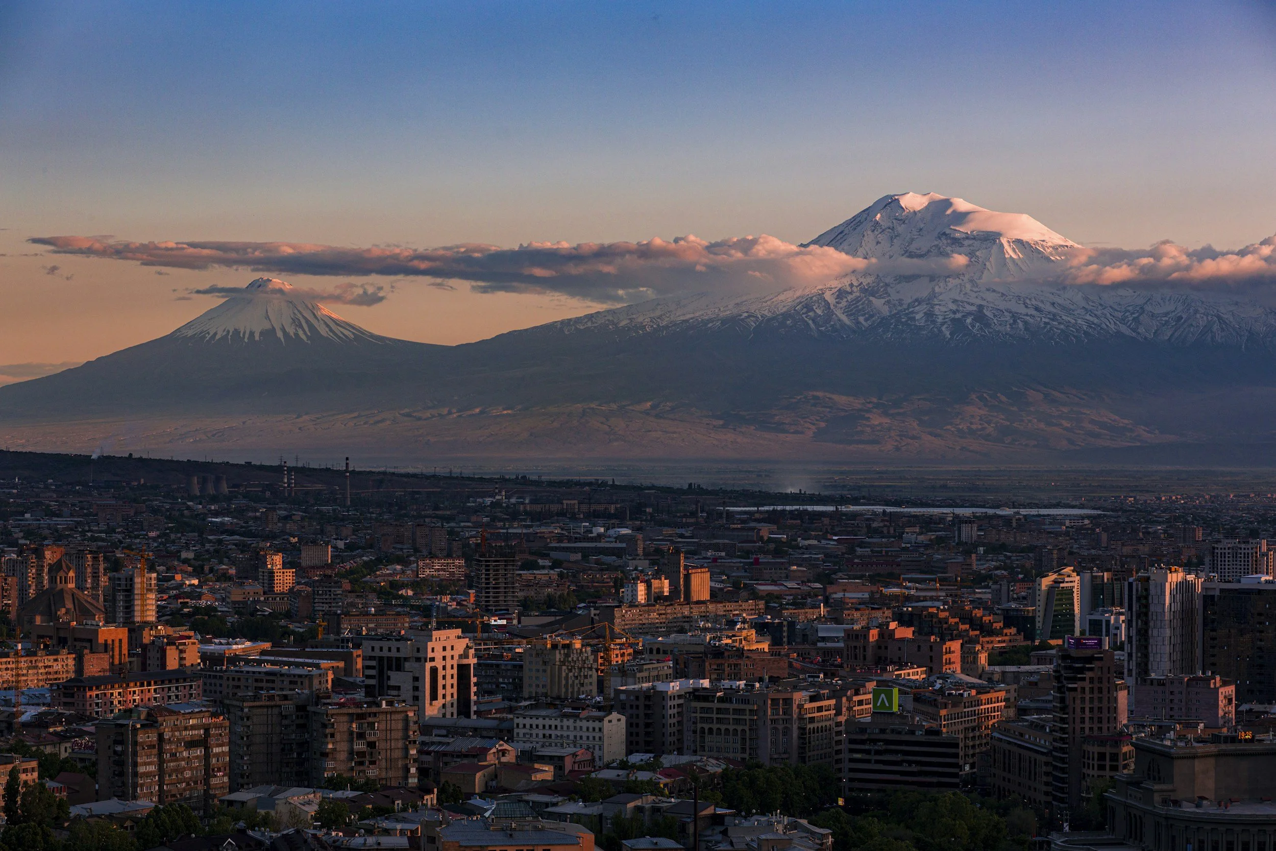 Aerial view of Yerevan city at golden hour with the twin snow-capped peaks of Mount Ararat rising above the horizon in the distance, Armenia