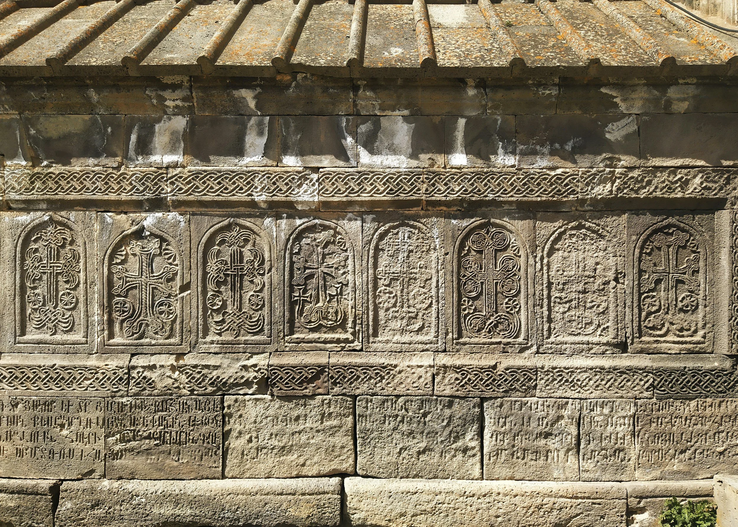 Close-up detail of intricately carved Armenian khachkar stone crosses with ornamental interlace patterns built into the wall of a medieval monastery