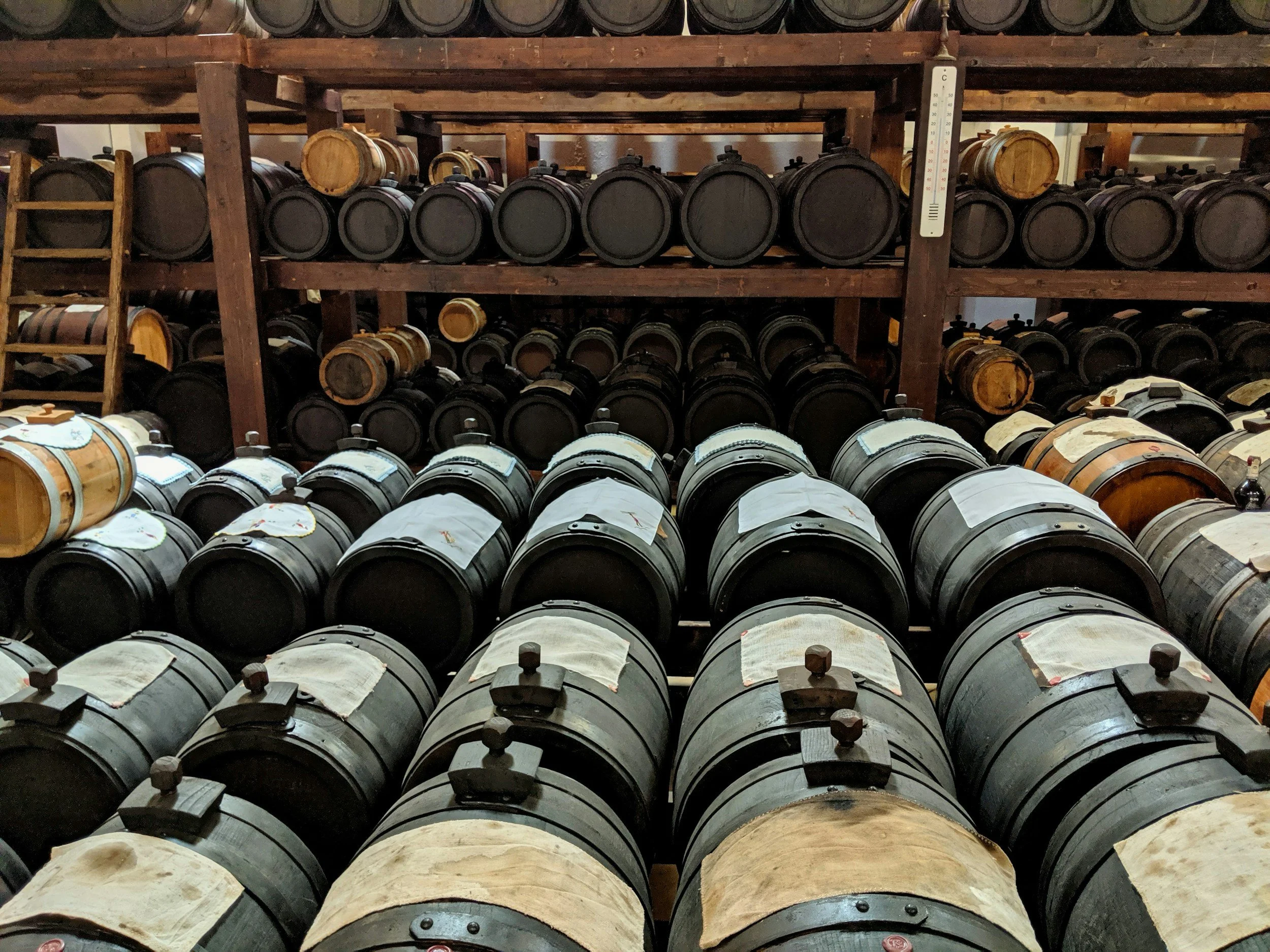 Rows of dark oak and chestnut barrels of different sizes used for aging traditional balsamic vinegar stacked on wooden shelves in an acetaia in Modena, Emilia-Romagna, Italy