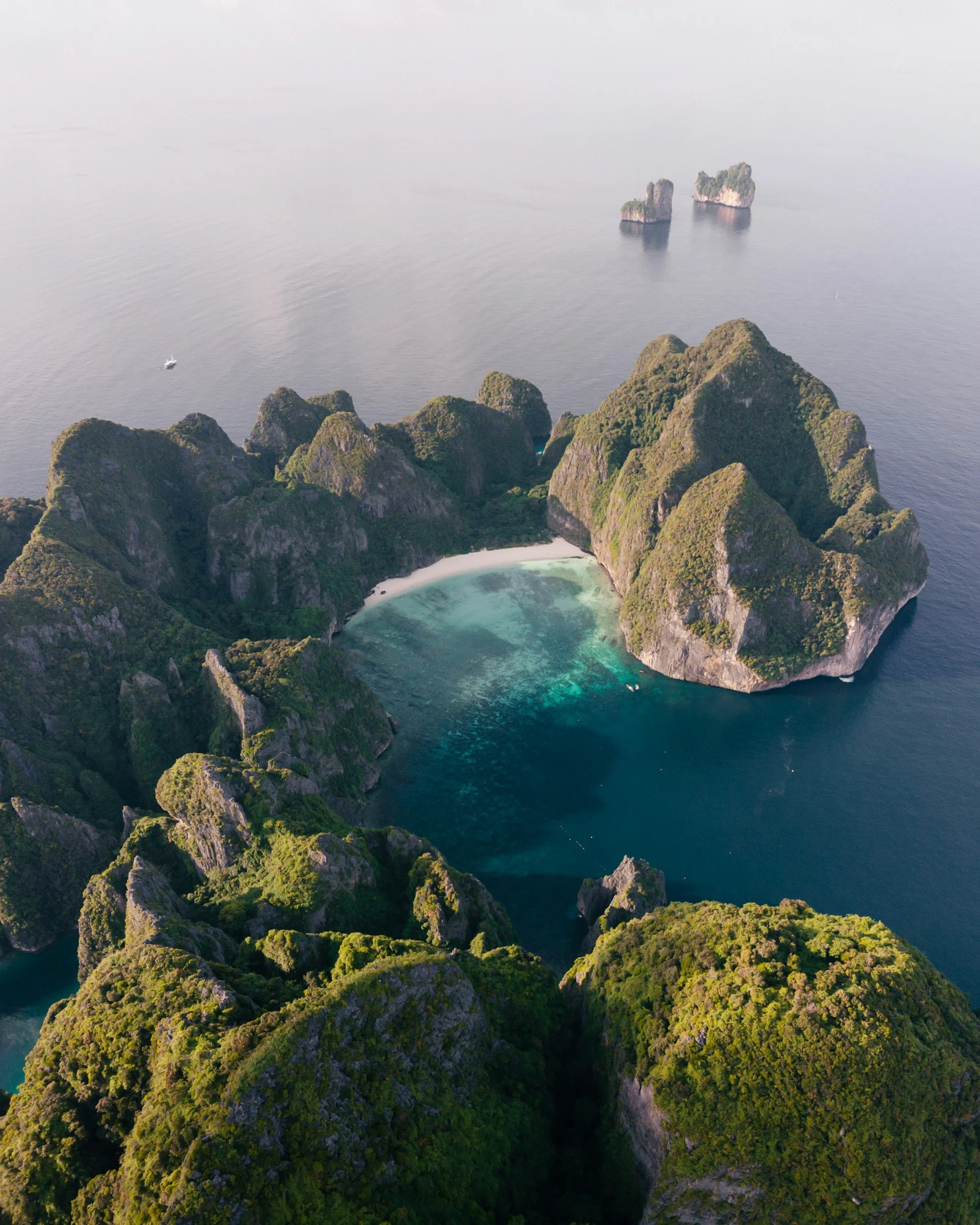 Aerial view of Phi Phi Island showing a hidden turquoise lagoon enclosed by steep forested limestone cliffs rising from the Andaman Sea, Thailand