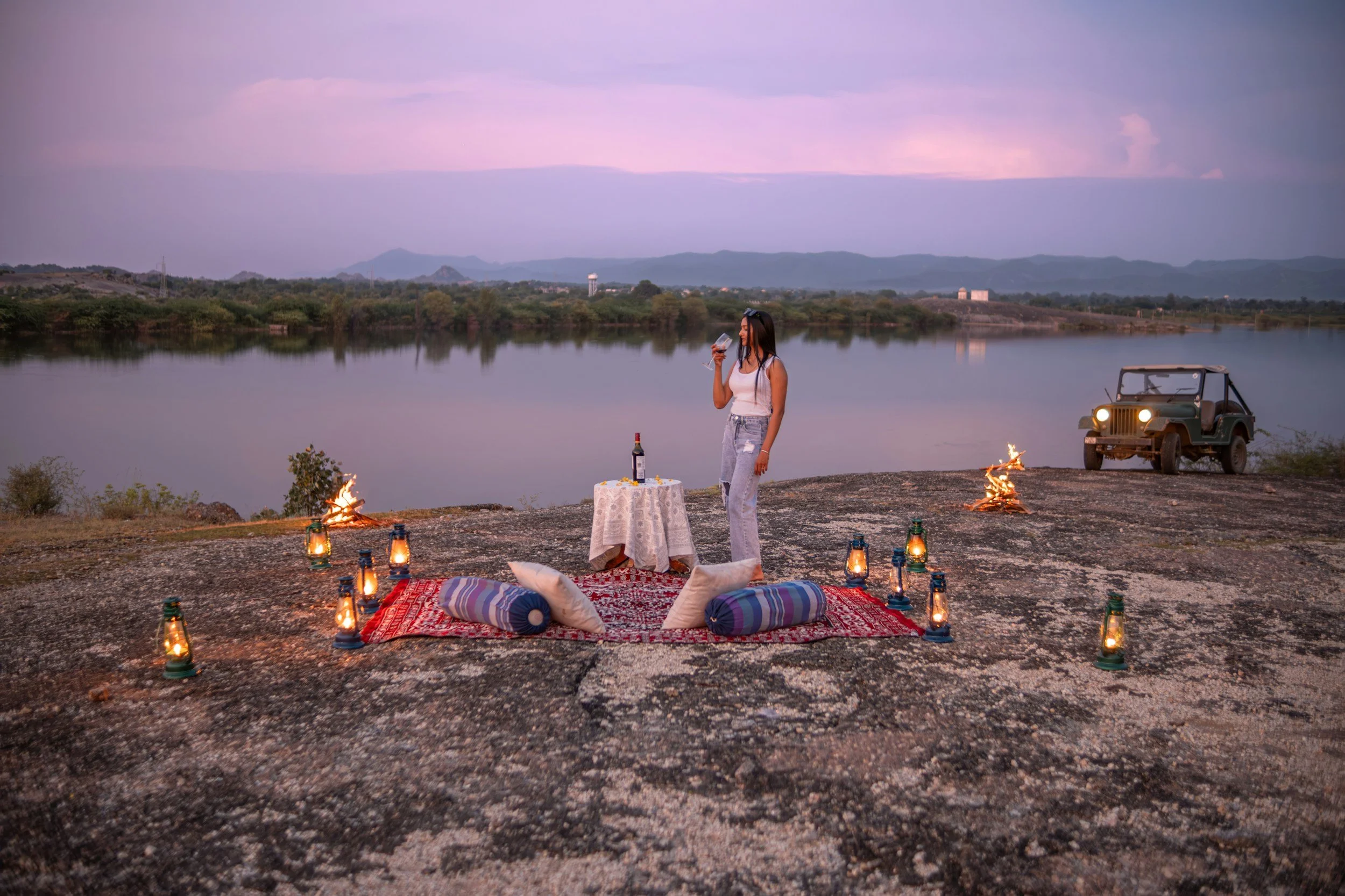 Guest standing at a private bush dinner table set with lanterns and candles on a rocky outcrop overlooking a lake at dusk in Kenya