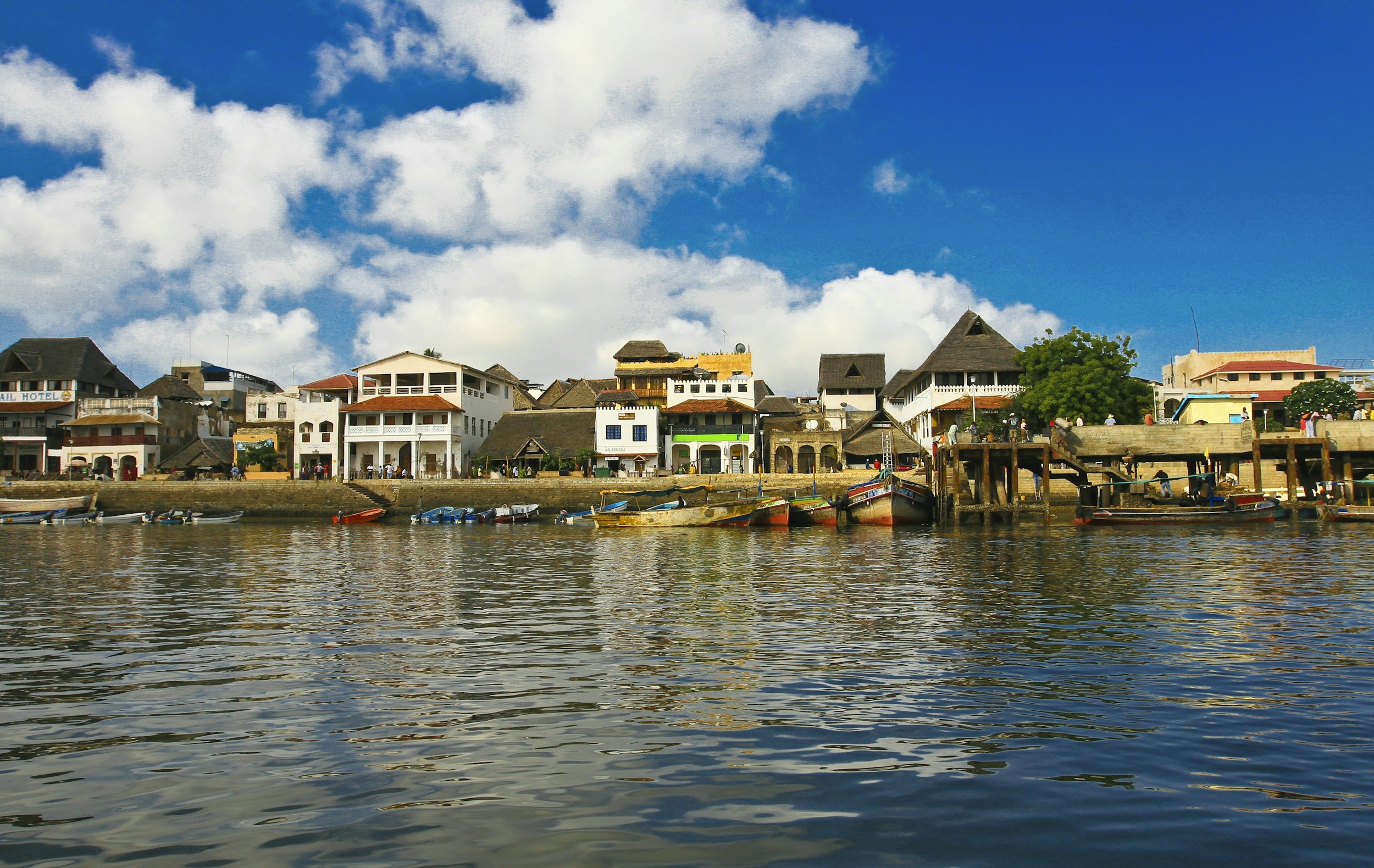 Colourful traditional boats moored along the Lamu waterfront with whitewashed Swahili architecture and a bright blue sky, Lamu Archipelago, Kenya