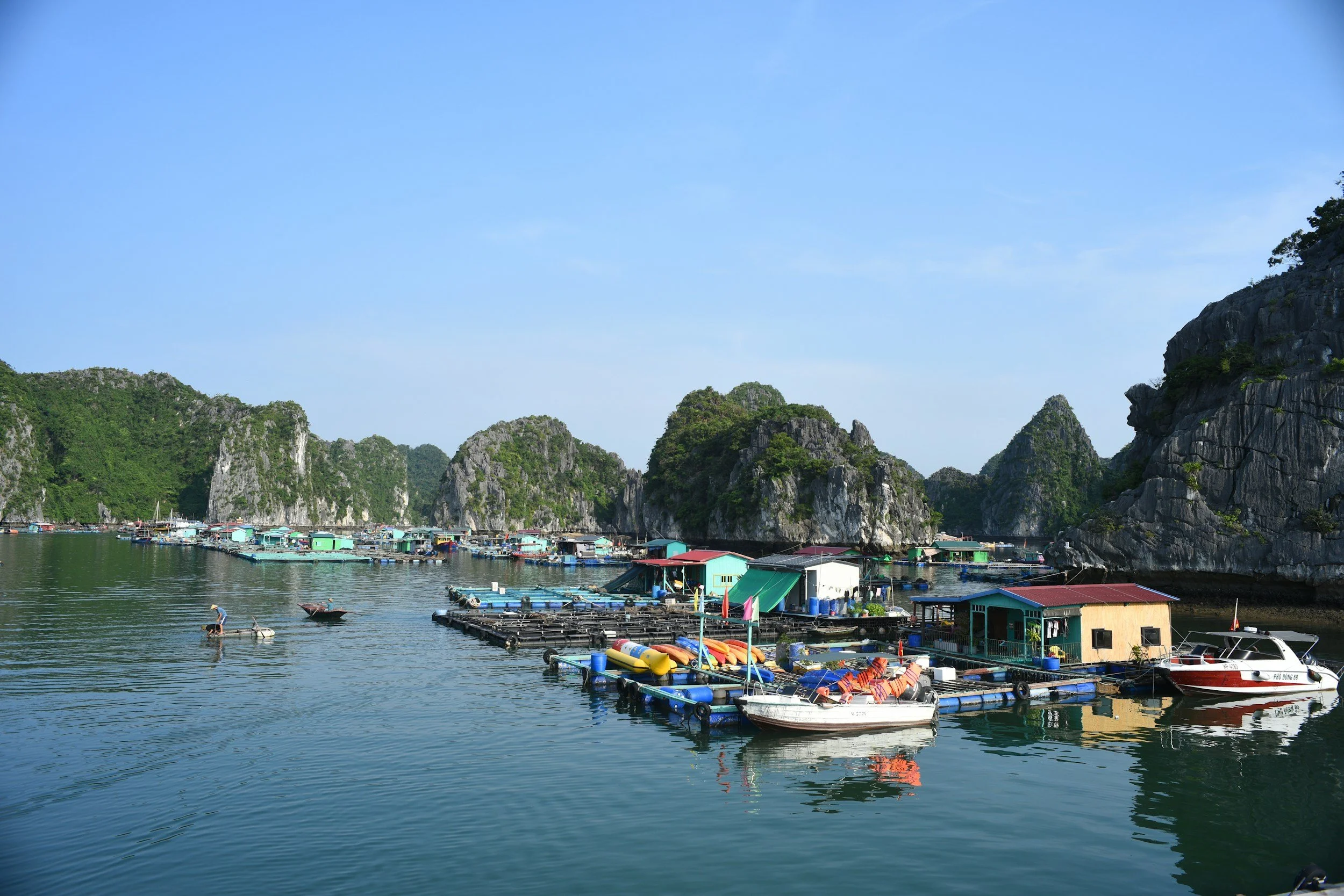 A colourful floating fishing village with wooden houses and fish farms moored between towering limestone karst cliffs in Ha Long Bay, Vietnam