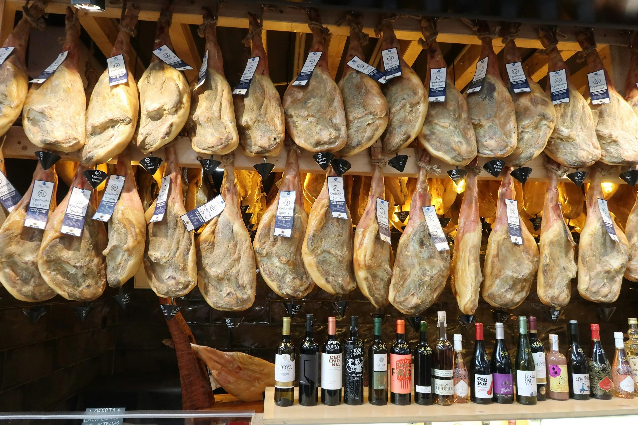 Rows of cured Ibérico ham legs hanging from the ceiling of a traditional Spanish charcuterie shop in Andalucía, Spain, with wine bottles displayed below