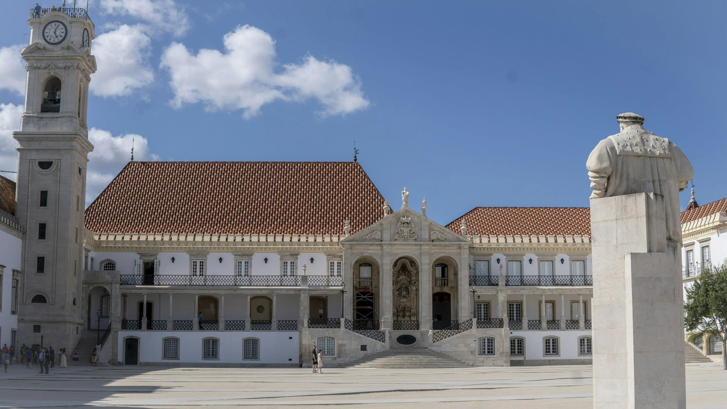 The baroque courtyard of the University of Coimbra with its ornate entrance portal, a statue in the foreground and blue sky above, one of the oldest universities in the world, Portugal