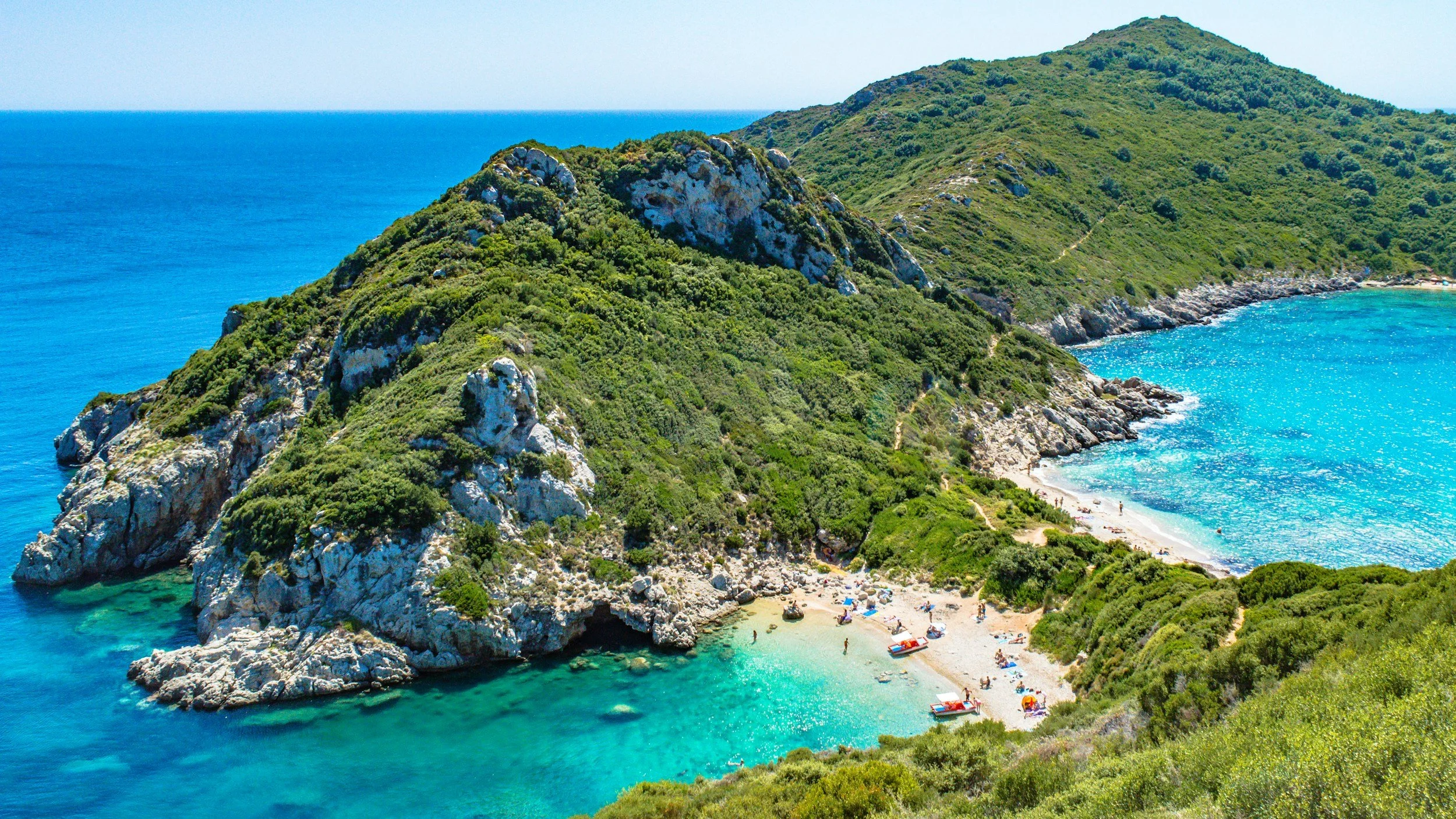 A secluded cove with a sandy beach, crystal-clear turquoise water and densely forested cliffs in the Ionian Islands, Greece, accessible only by private boat