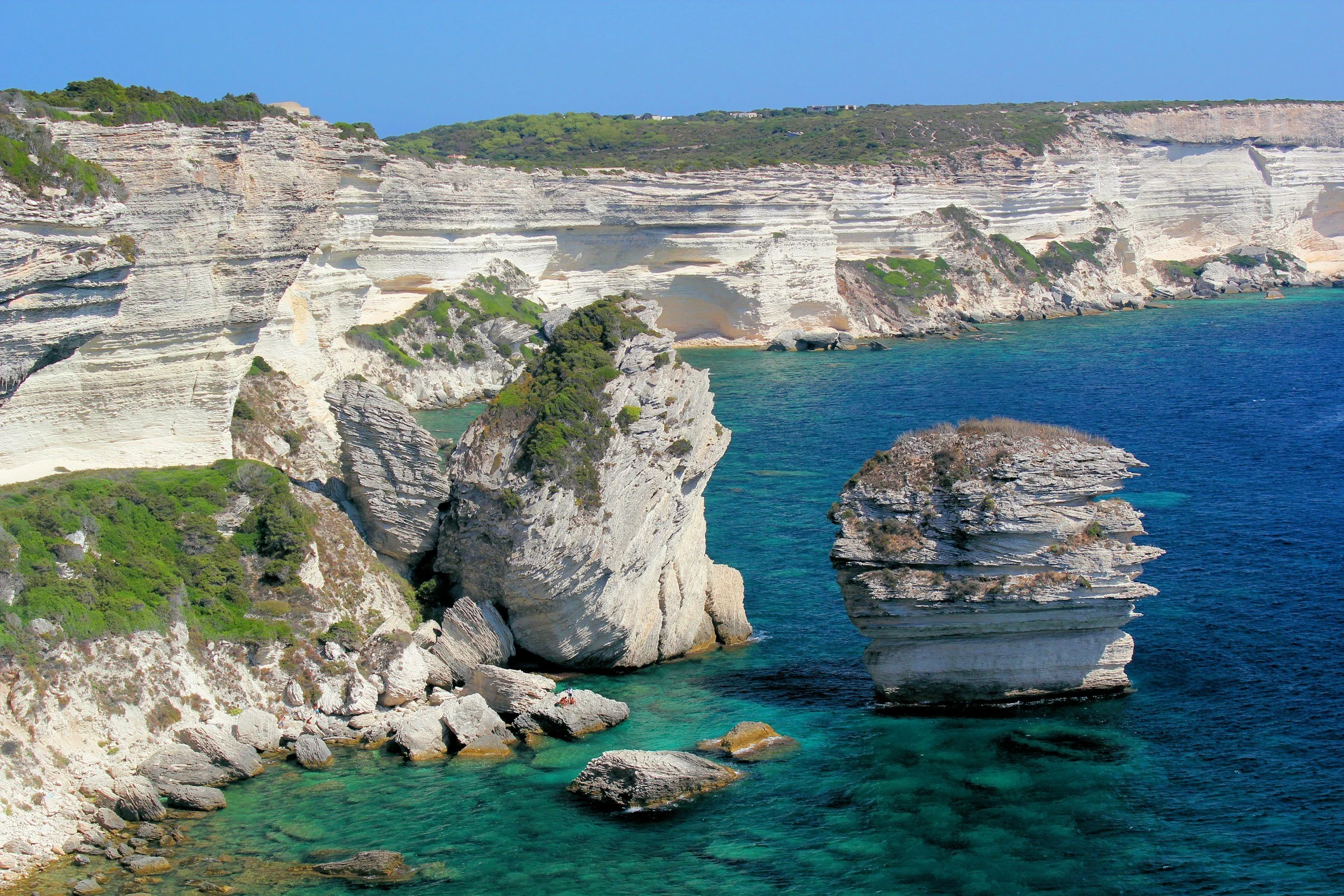 Dramatic white limestone sea cliffs and rock stacks rising from the turquoise Mediterranean at Bonifacio, Corsica, France