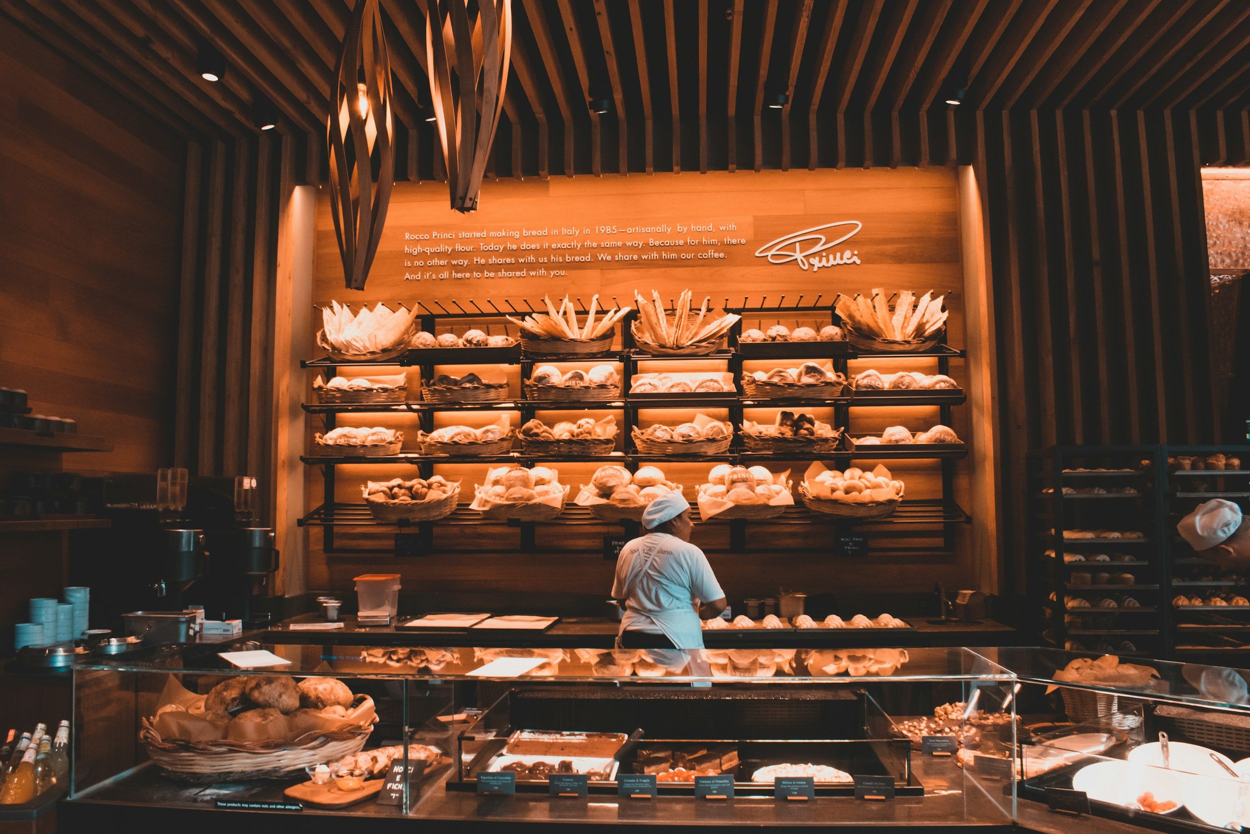 A baker in a white toque working behind a counter lined with pastries and breads at a classic Paris patisserie and boulangerie, France