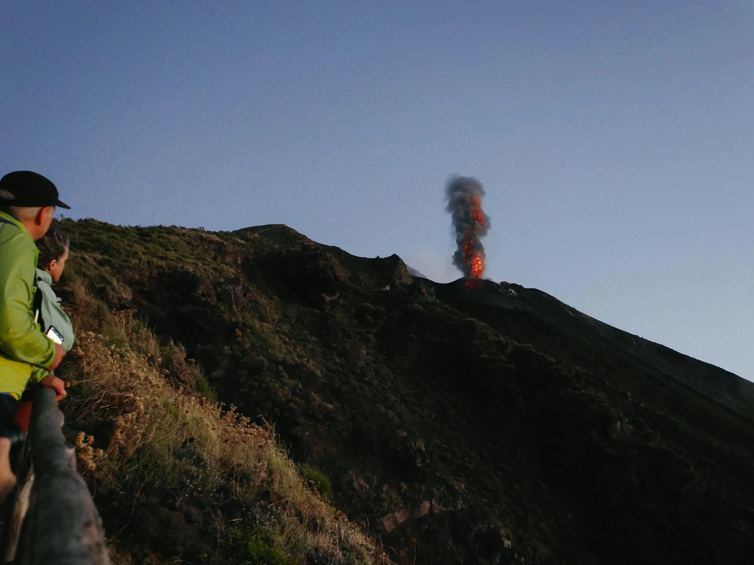 Stromboli volcano actively erupting with a plume of smoke rising from the crater, with a 4x4 vehicle on the dark lava slopes, Aeolian Islands, Sicily, Italy
