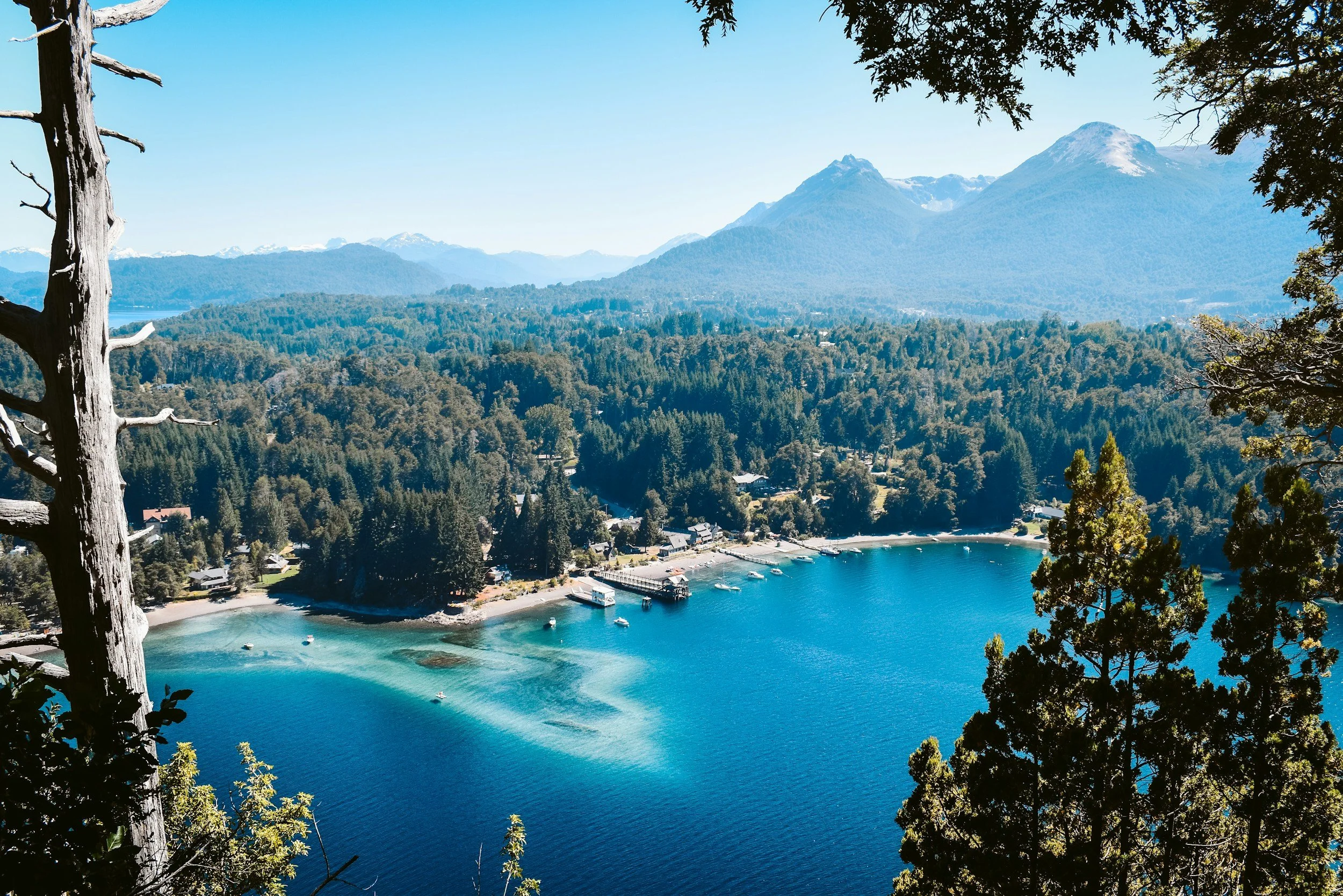 Aerial view of the turquoise Nahuel Huapi lake with dense native forest and a small marina, in the Argentine Lake District near Bariloche, Argentina