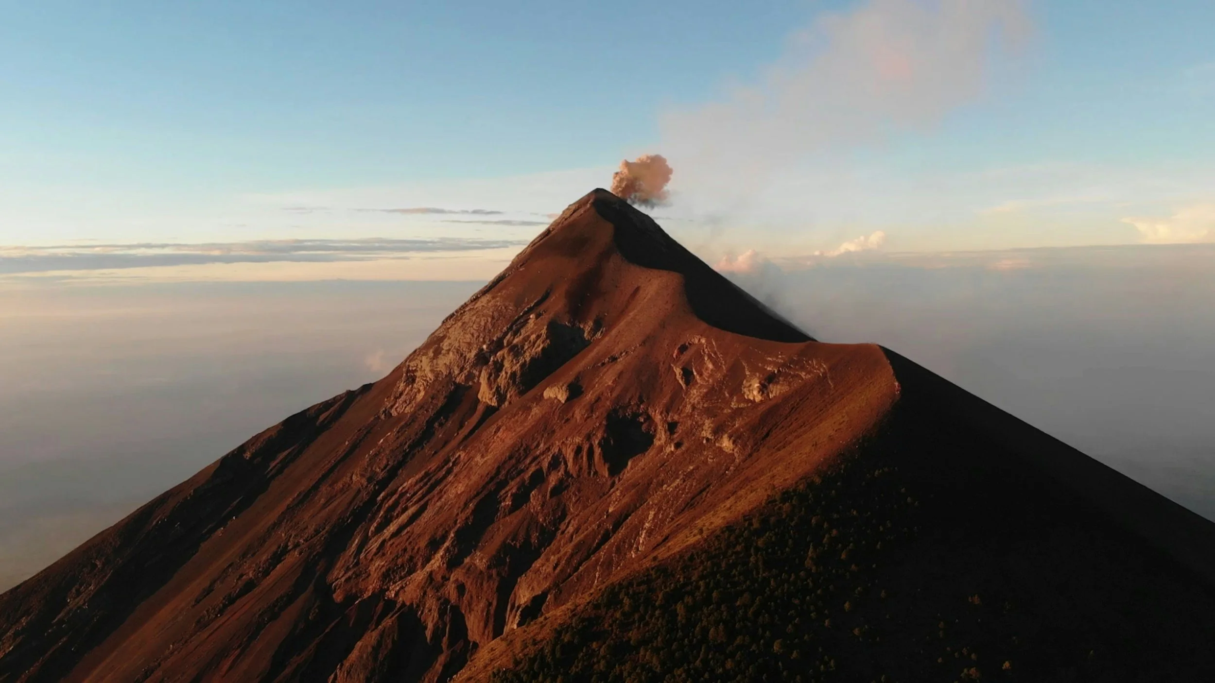 Acatenango volcano summit glowing with smoke and ash against a dramatic orange and purple dusk sky on an overnight hike in Guatemala