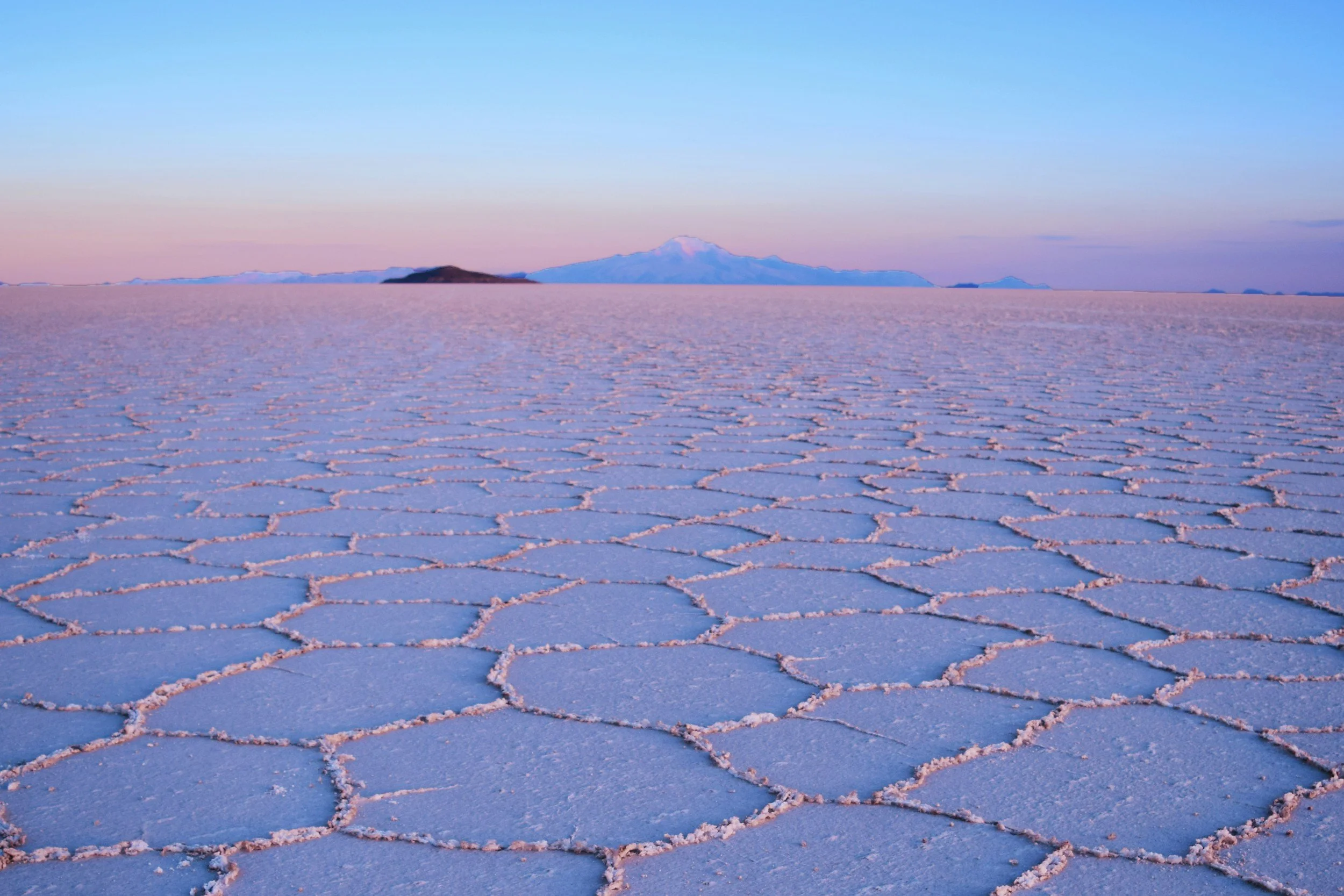 Infinite hexagonal salt crust of the Salar de Uyuni stretching to the horizon under a pink and blue dusk sky in Bolivia