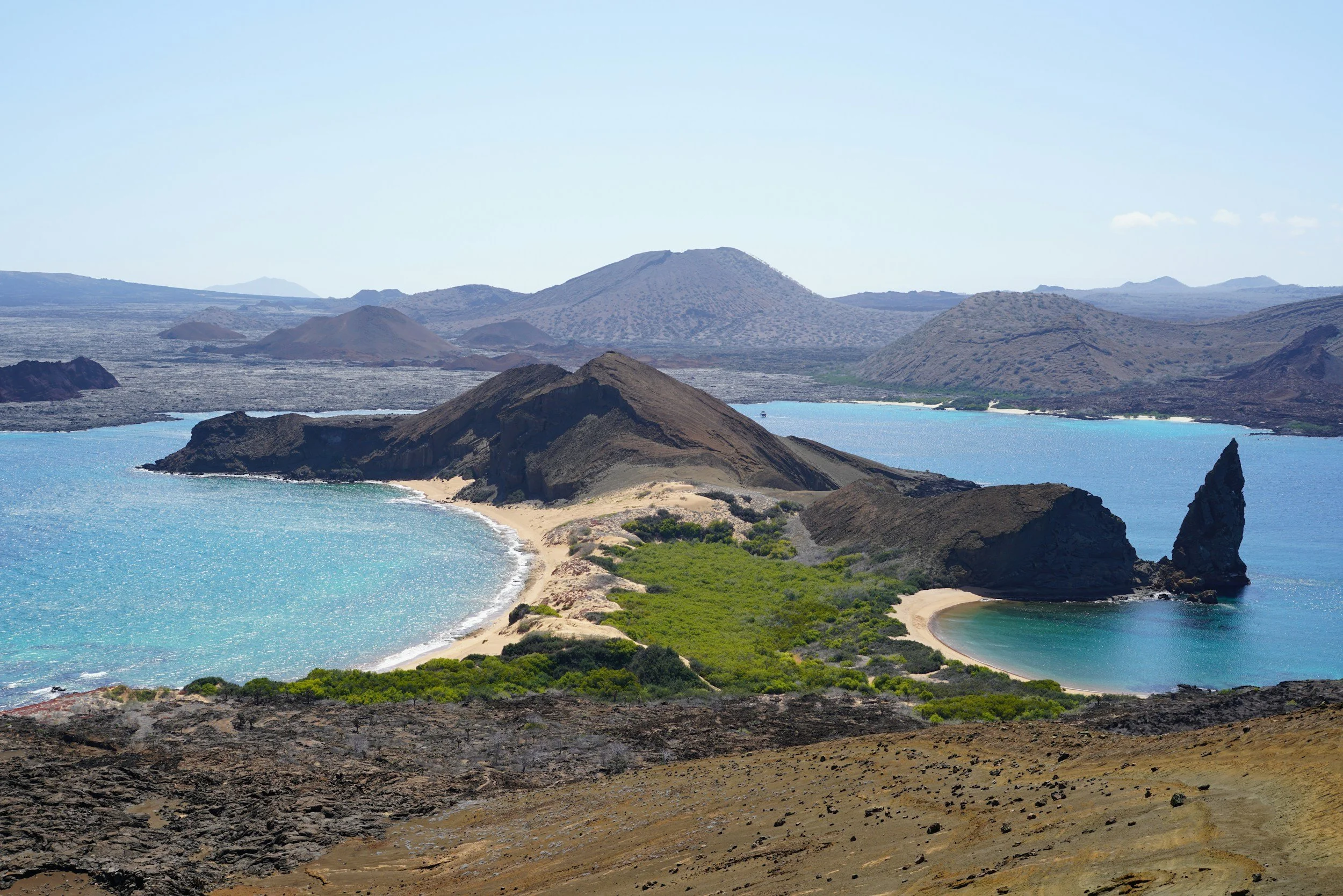 Iconic Pinnacle Rock rising above a volcanic bay on Bartolomé Island in the Galápagos, with turquoise water and a sandy beach below, Ecuador