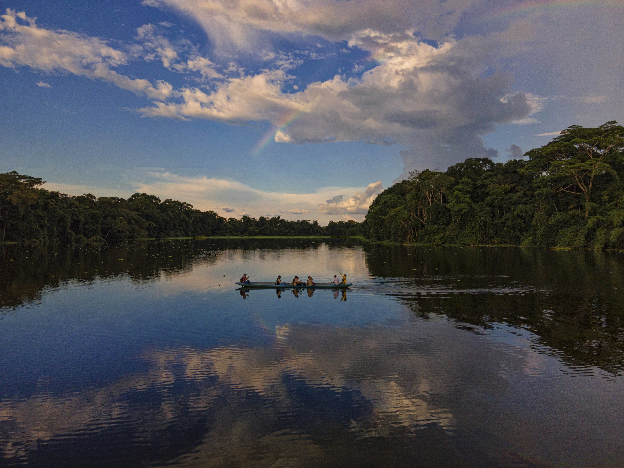 Small canoe with travellers gliding across a calm jungle lake surrounded by dense Amazon rainforest under a dramatic sky in Ecuador